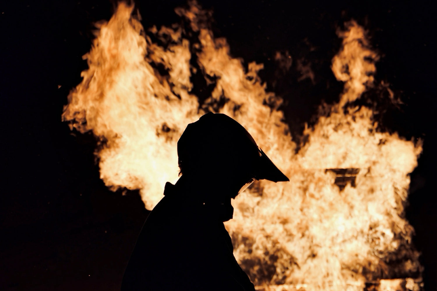 Silhouette of a person wearing a cap against a fiery background