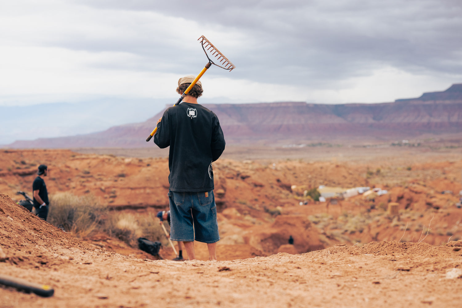 Person holding a rake in a desert landscape with mountains in the background
