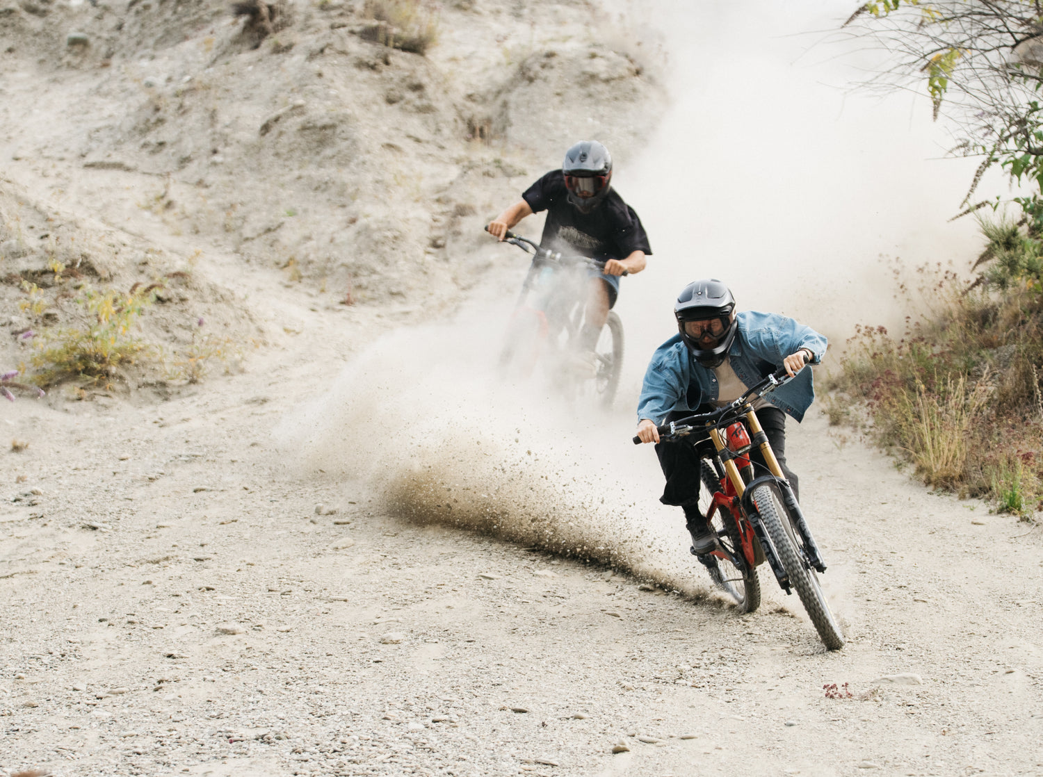 Two people riding mountain bikes on a dirt trail with dust in the air.