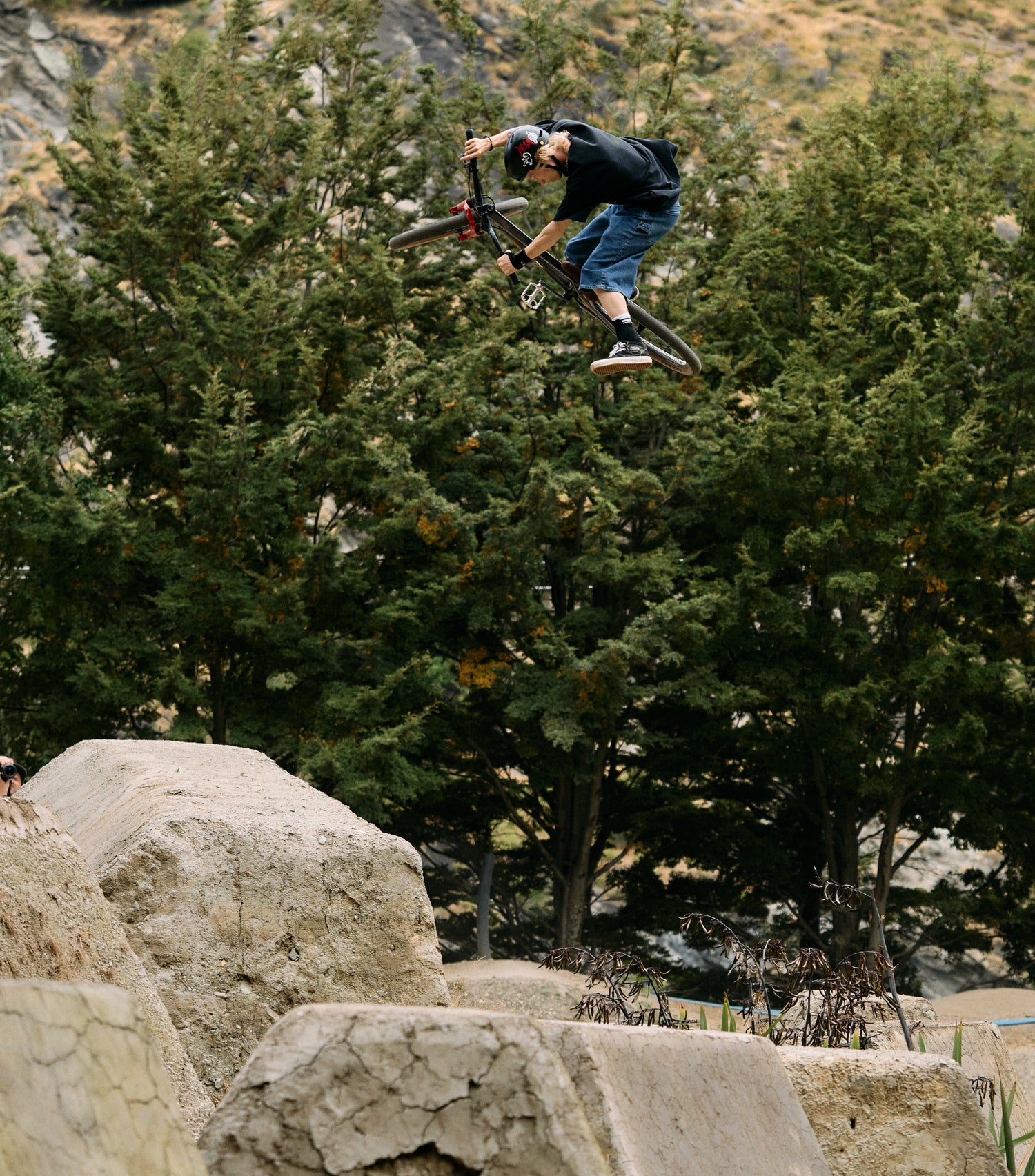 Person performing a bike trick in mid-air with trees and rocks in the background