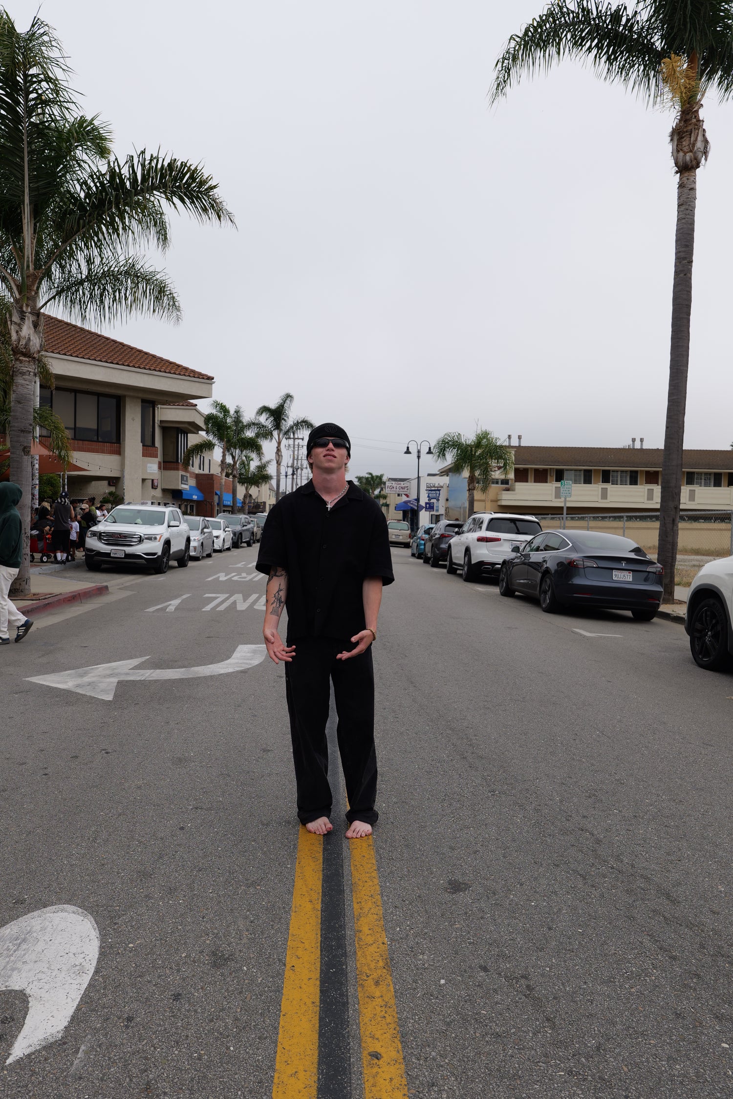 Person standing on a street with palm trees and buildings in the background