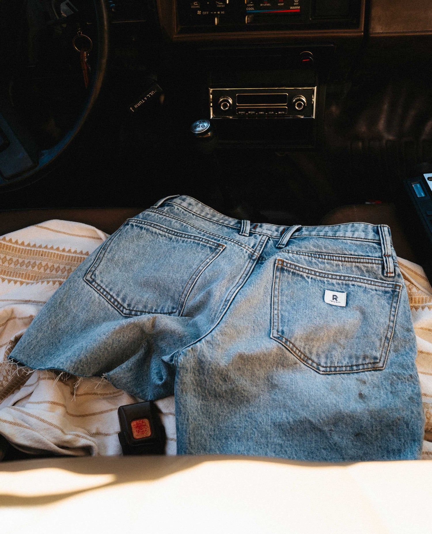 Light blue denim shorts placed on a blanket inside an old truck.