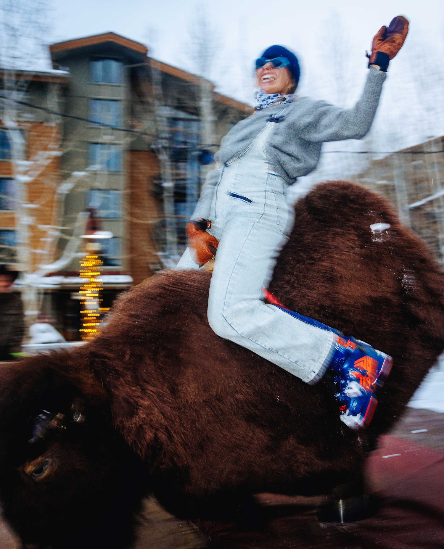Person riding a large brown dog in an urban setting with buildings and snow.