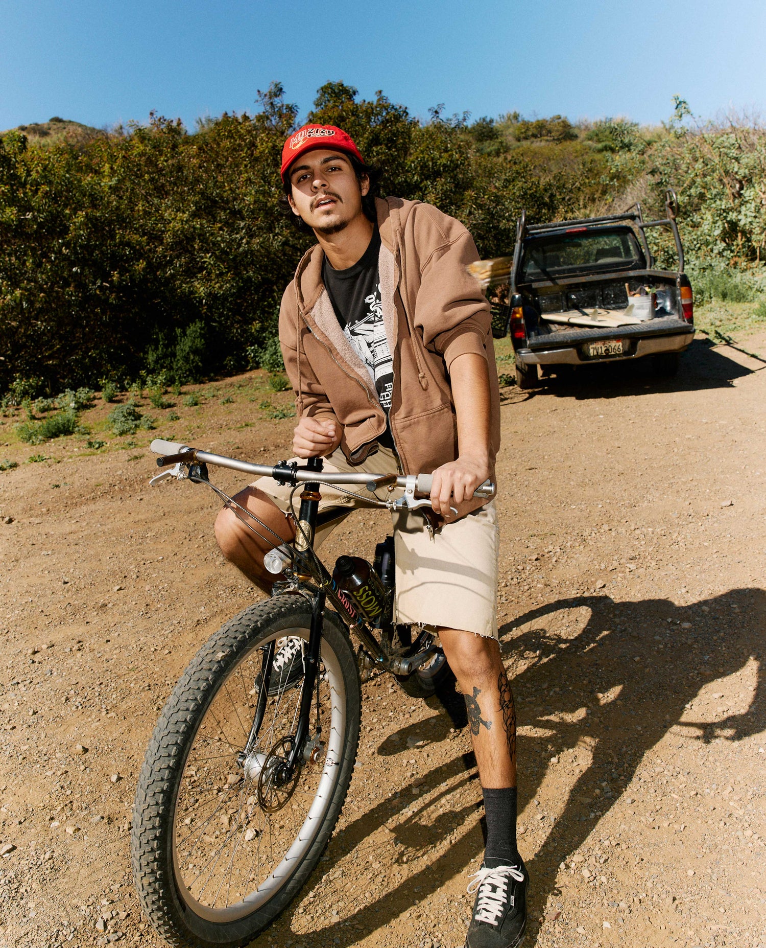 Man with a bicycle on a dirt road with a vehicle in the background