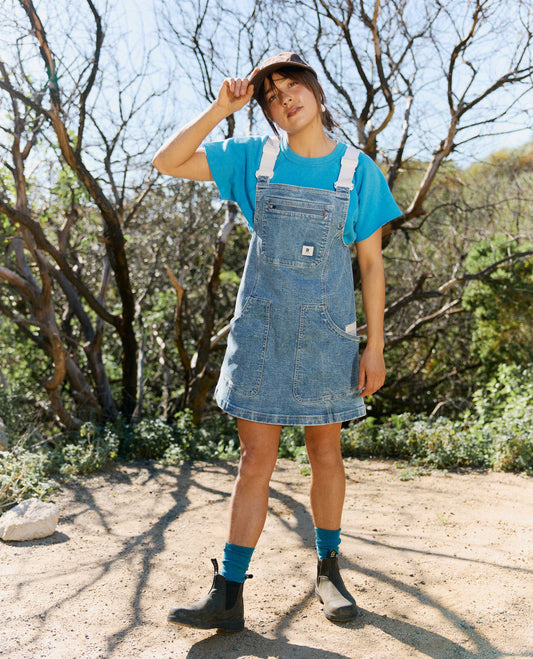 Person wearing a blue denim dress over a t-shirt in a natural setting