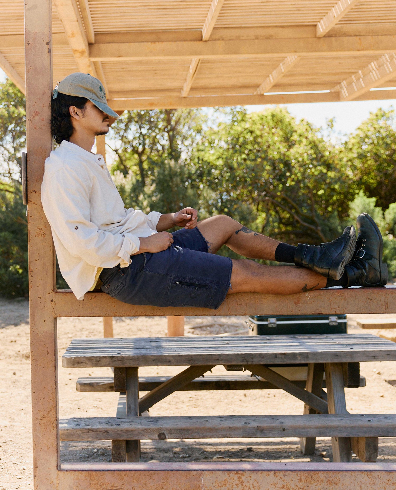 Person sitting on a wooden bench under a shelter with trees in the background