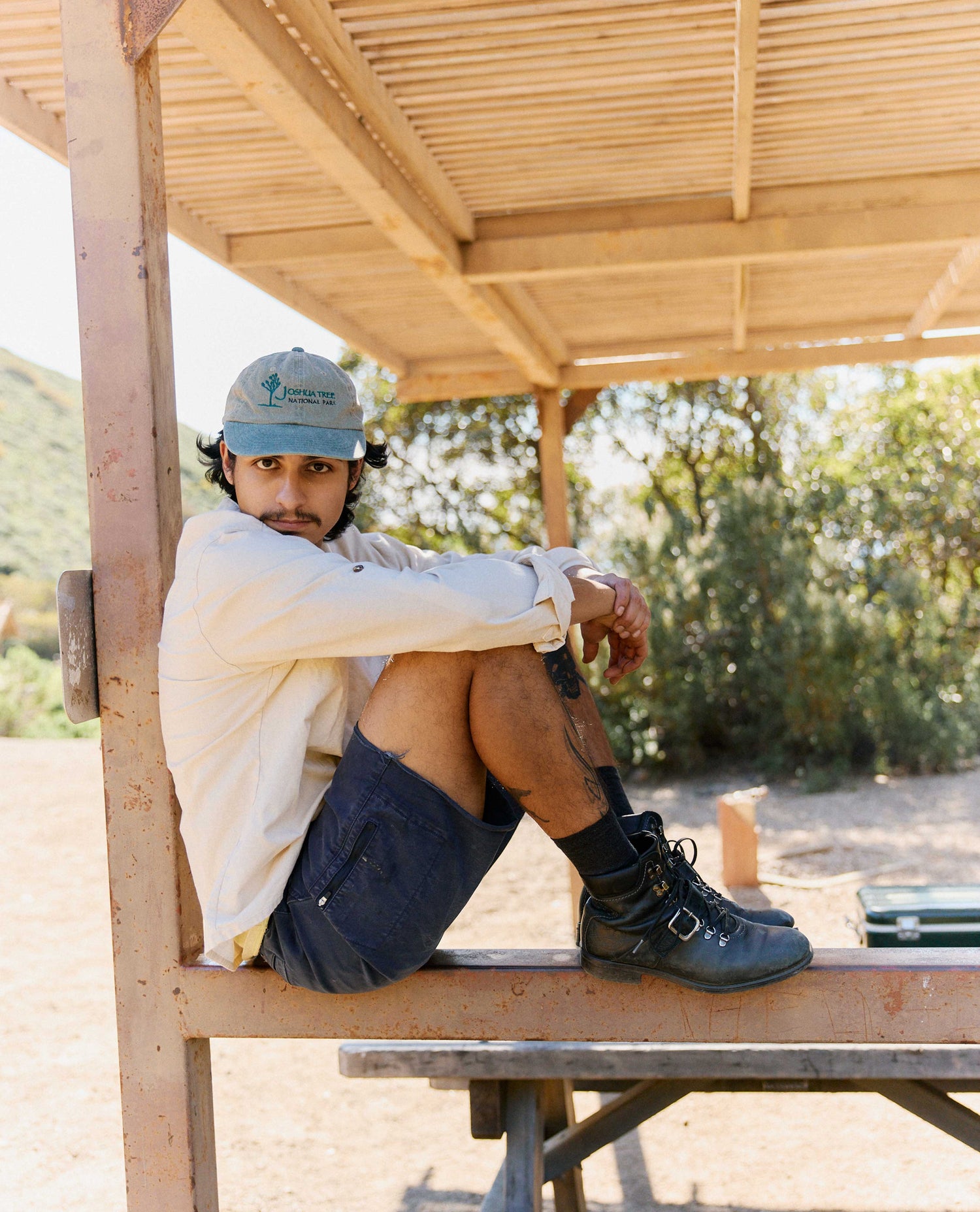 Person sitting on a wooden bench under a wooden shelter with trees in the background