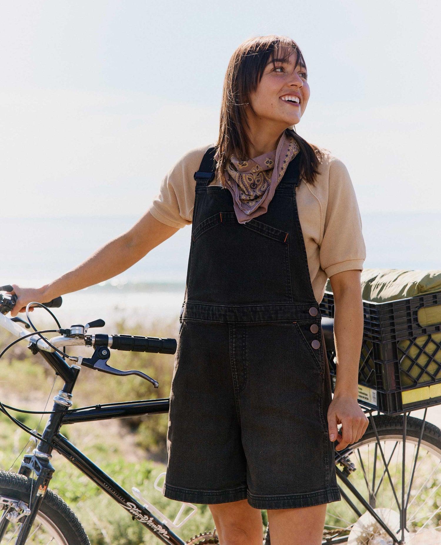 Woman in black overalls standing next to a bicycle with a scenic background