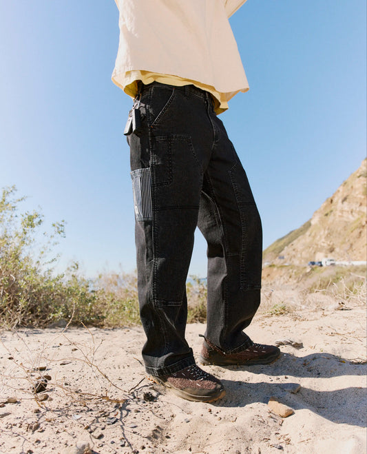 Person wearing black pants and a beige shirt standing in a desert-like environment with clear blue sky.