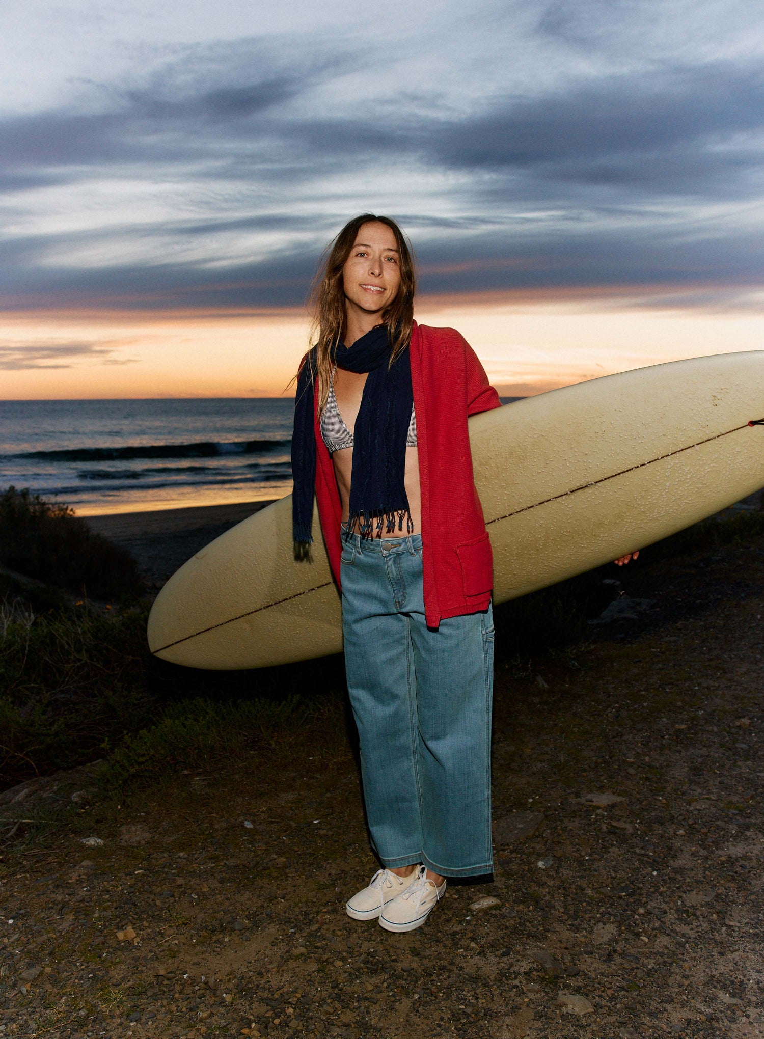 Person holding a surfboard on a beach at sunset