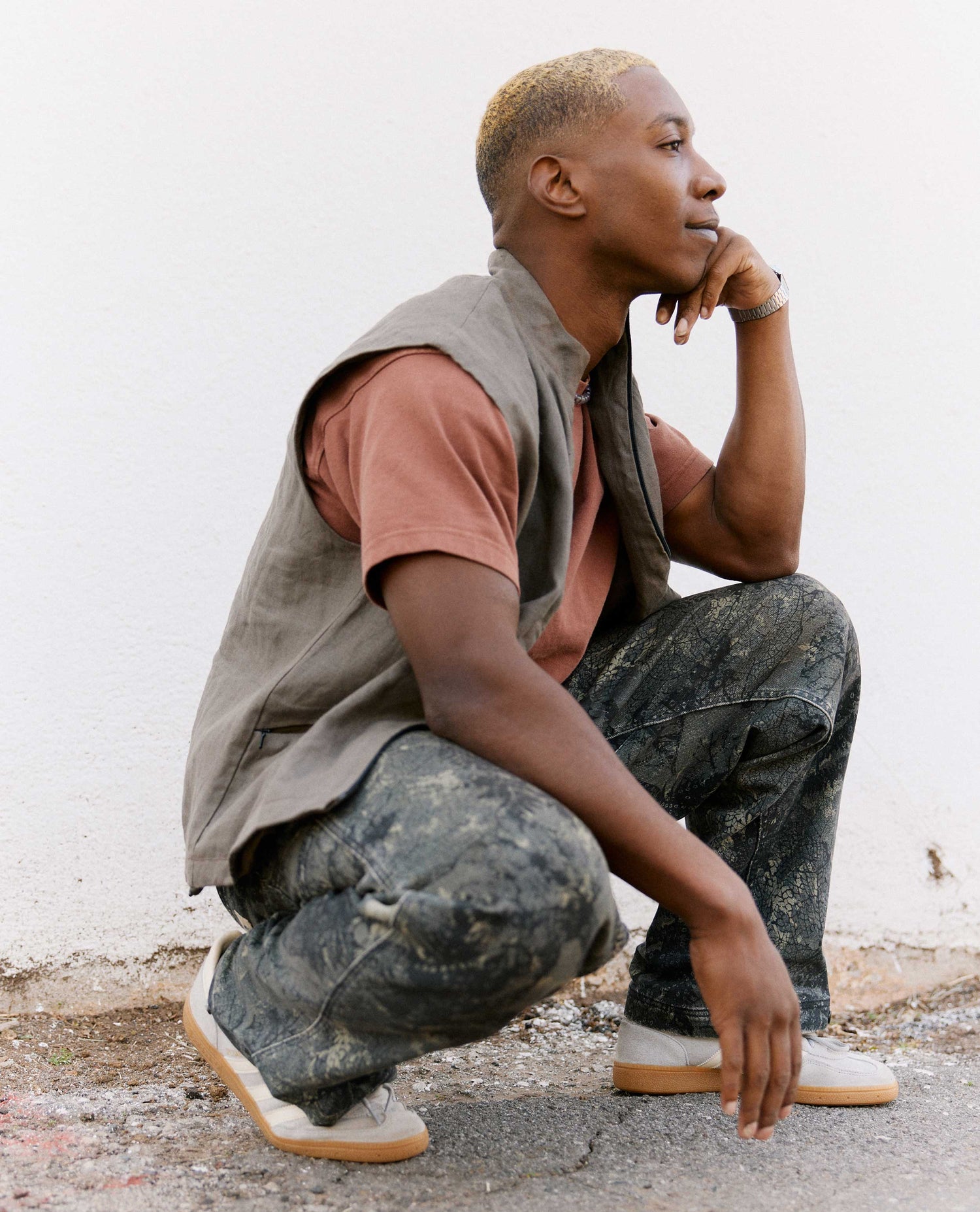 Person wearing a sleeveless vest and camouflage pants, sitting on the ground.