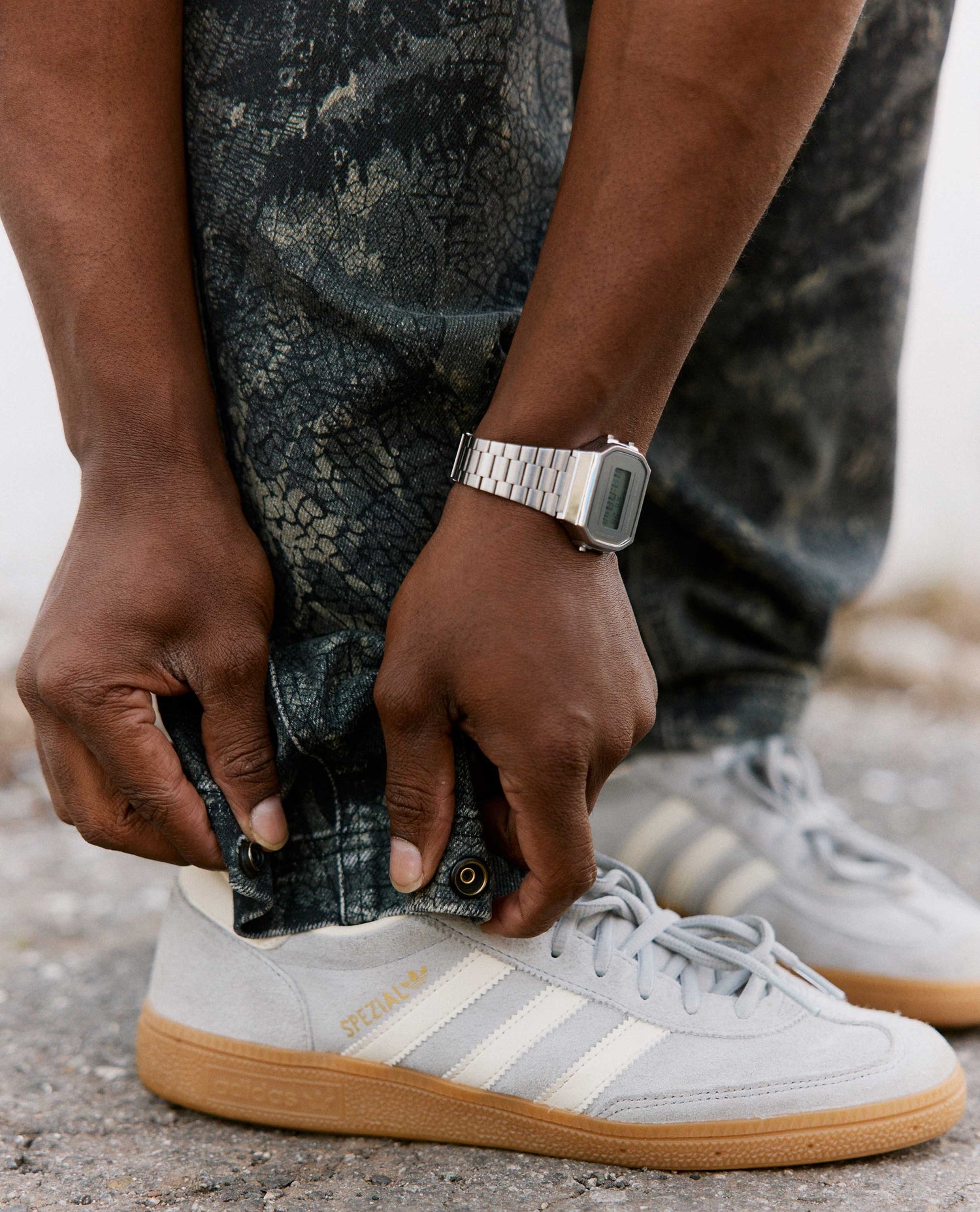 Person adjusting a shoe with a watch on wrist, wearing camouflage pants.
