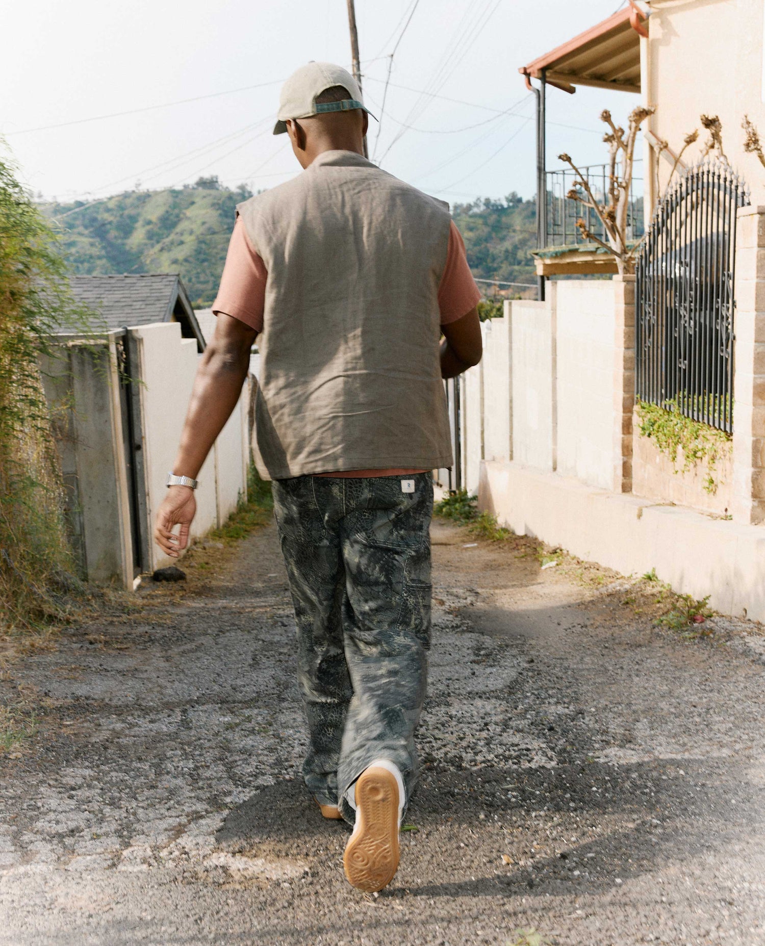 Man walking away from the camera on a narrow street with mountains in the background