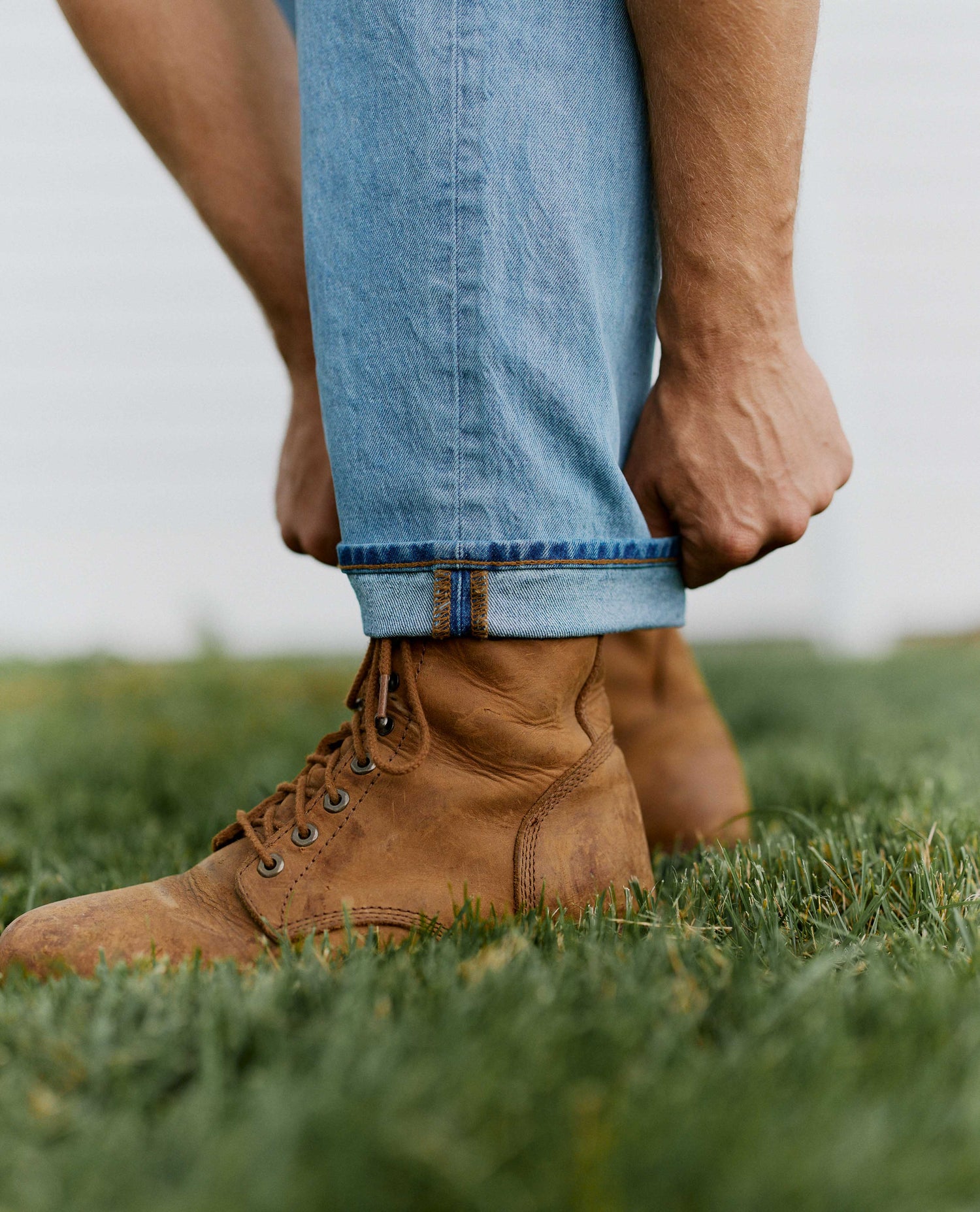Man adjusting the cuff of his blue jeans wearing leather boots