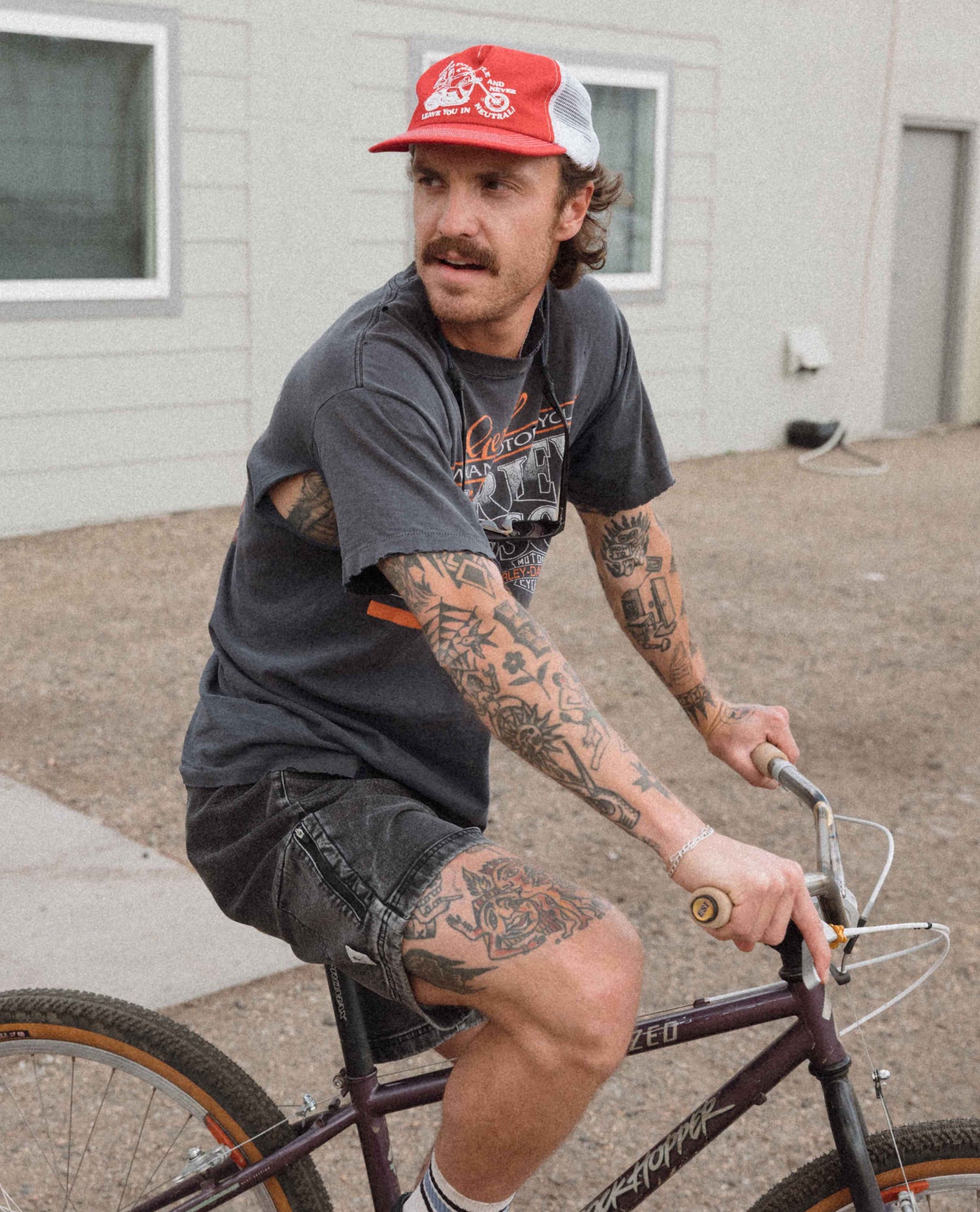 Man with tattoos riding a bicycle wearing a red and white cap.