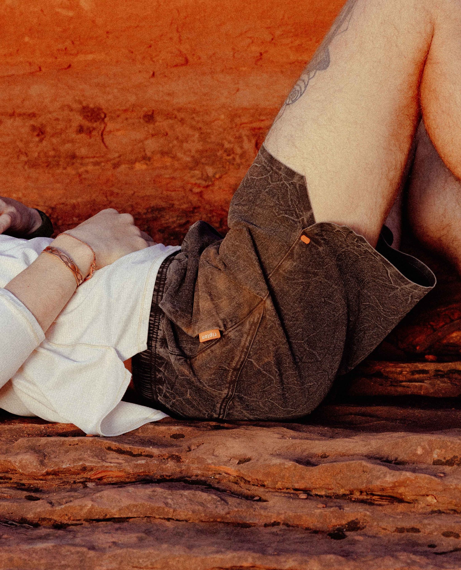 Person wearing brown leather shoes and white pants sitting on a red-brown surface.