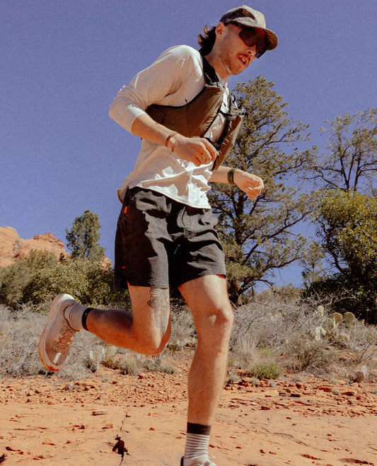 Person running on a dirt path in a natural landscape with trees and clear sky.