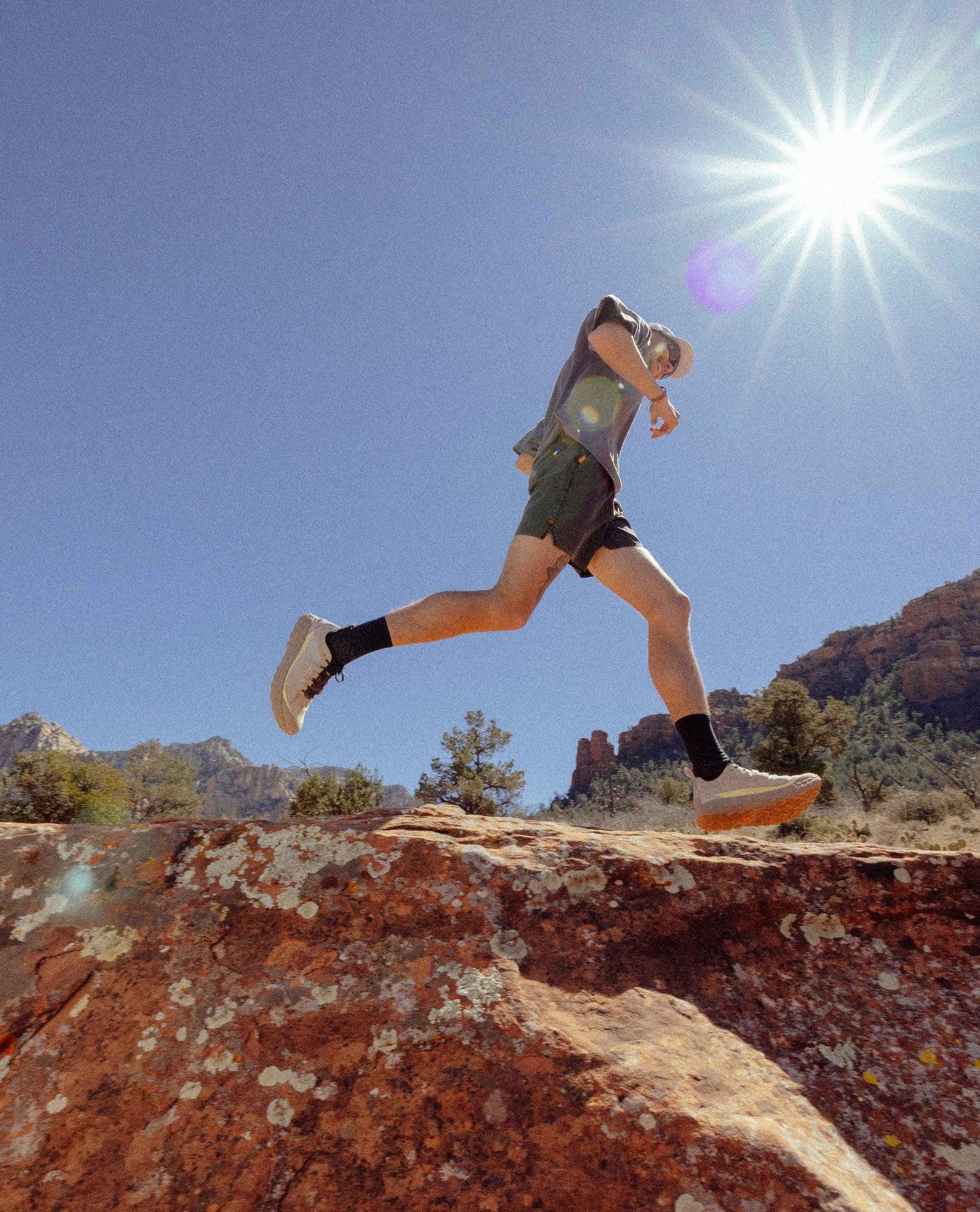 Person running on a rocky outcrop with a bright sun in the background
