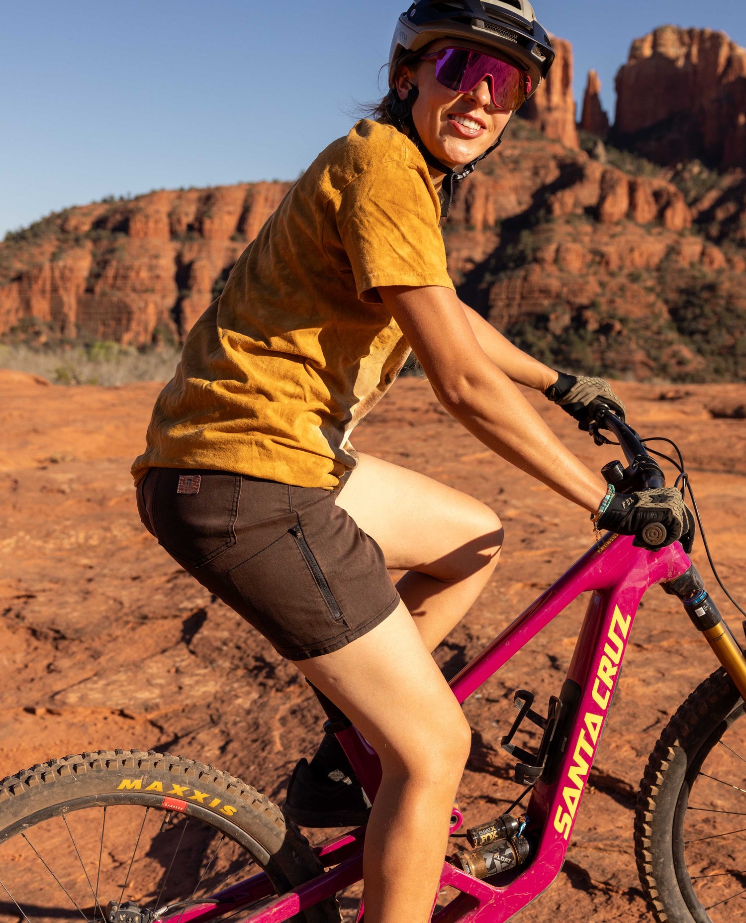 Person riding a pink Santa Cruz bike in a desert landscape with red rock formations.