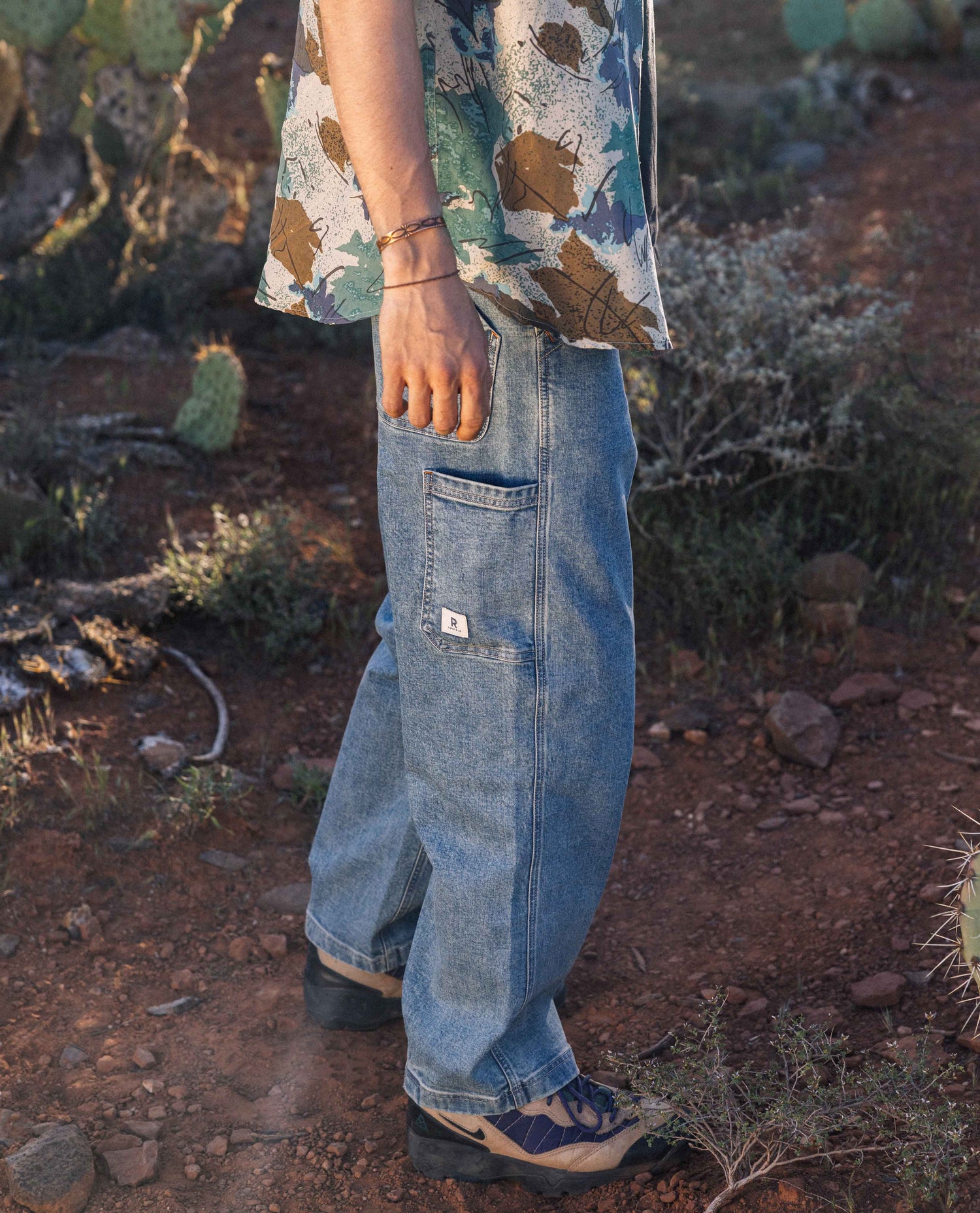 Man's legs in blue jeans with multi-color shirt standing in desert