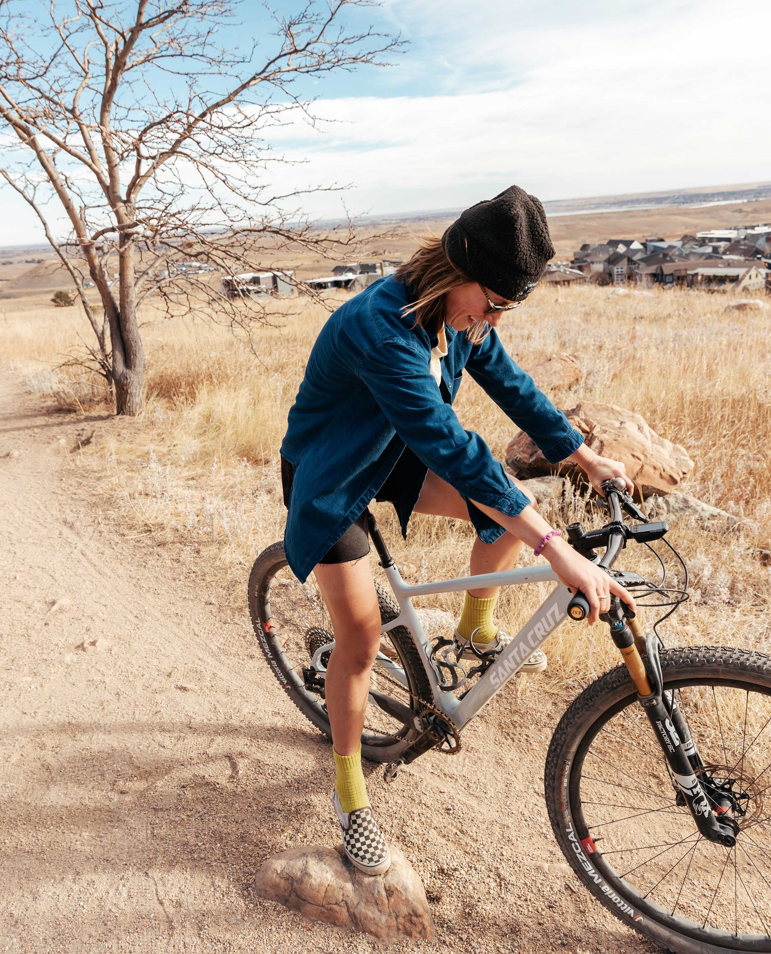 Girl on bike with blue shirt, black shorts, outside on a gravel trail with tree in background