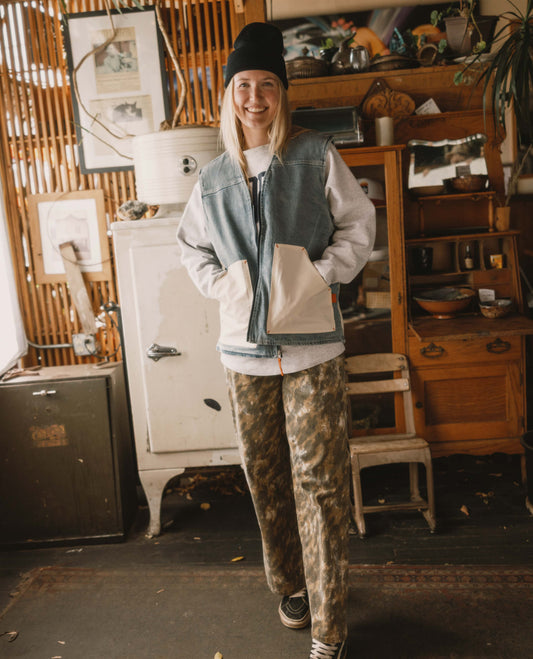 Person wearing a denim vest and camouflage pants in a rustic indoor setting