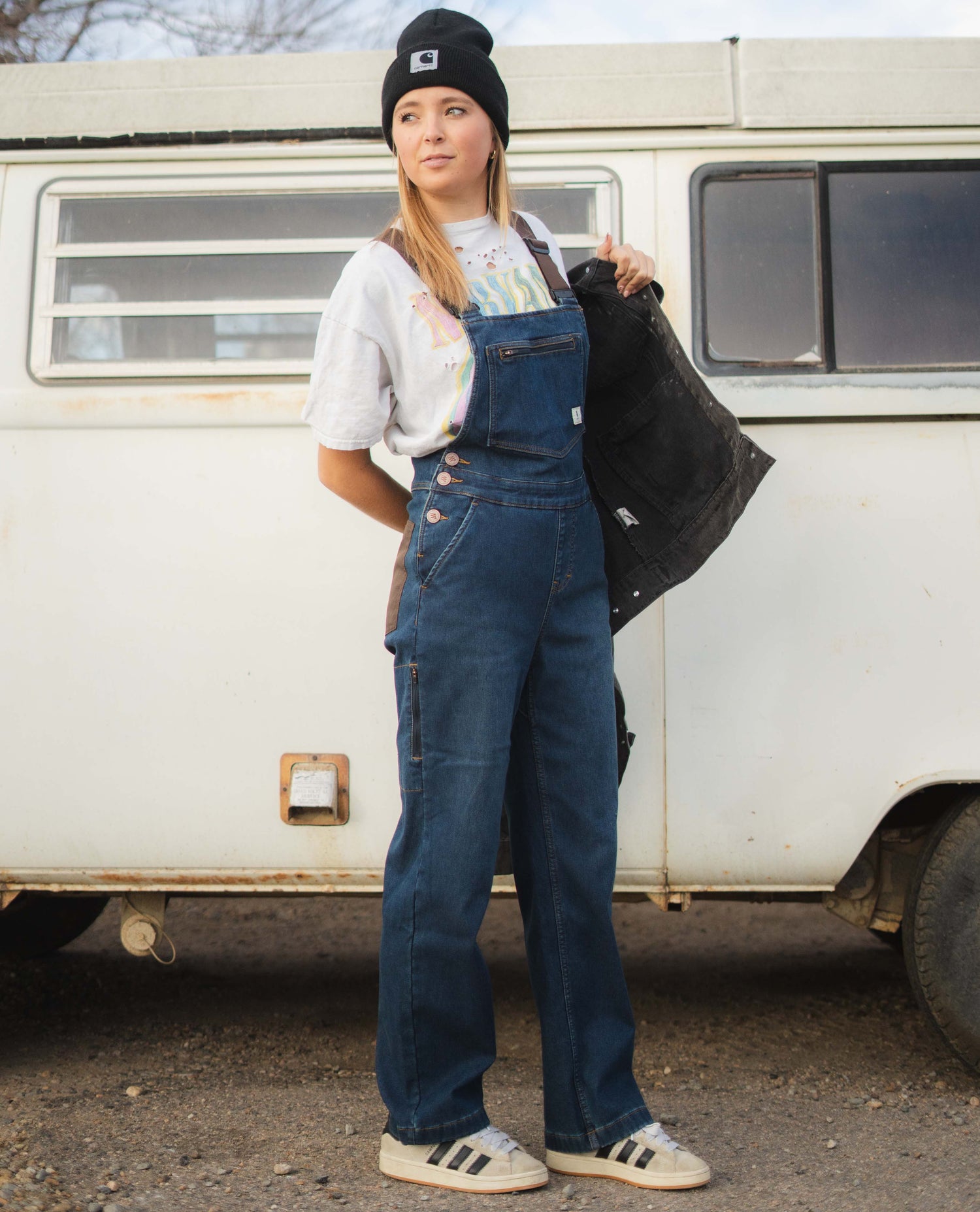 Person wearing blue denim overalls standing in front of a vintage van.