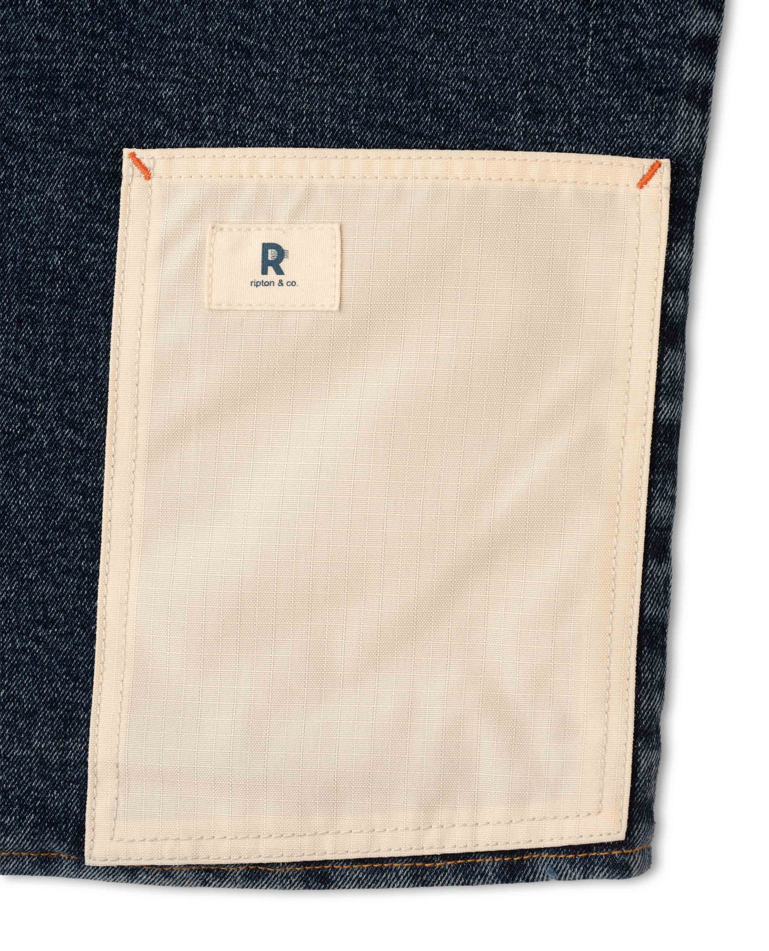 Close-up of a denim pocket with a beige patch and a brand logo on a white background
