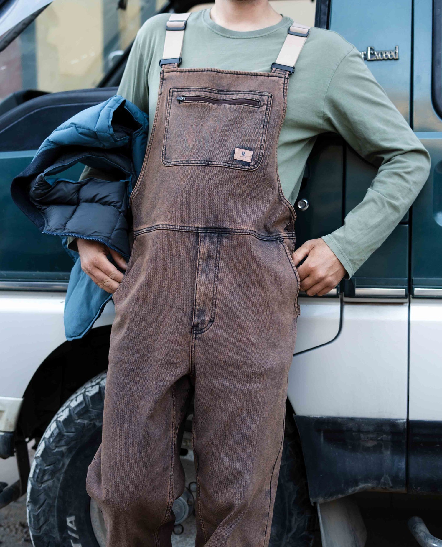 Person wearing brown overalls standing next to a vehicle