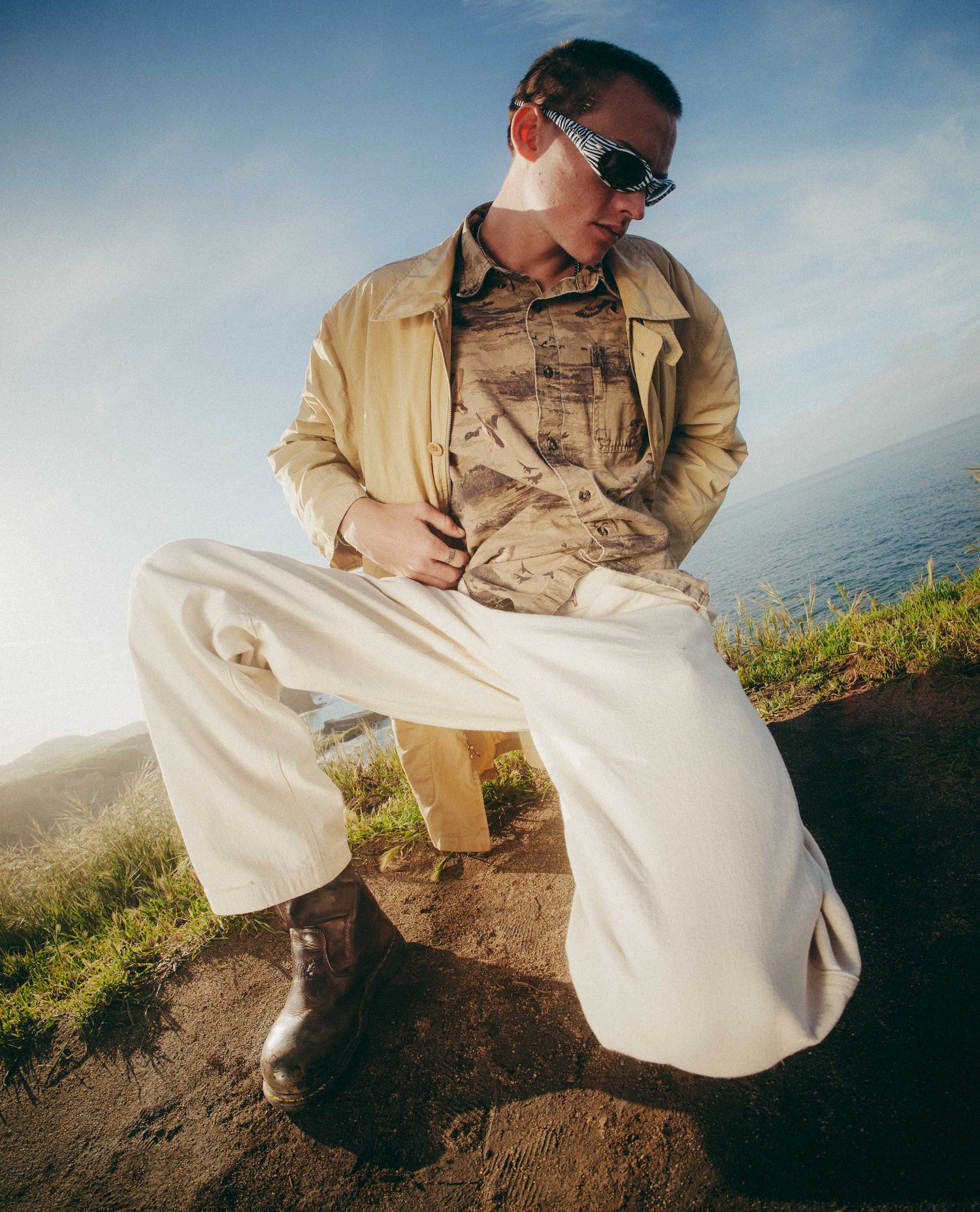 Person in outdoor setting wearing a beige jacket, camouflage shirt, and white pants.