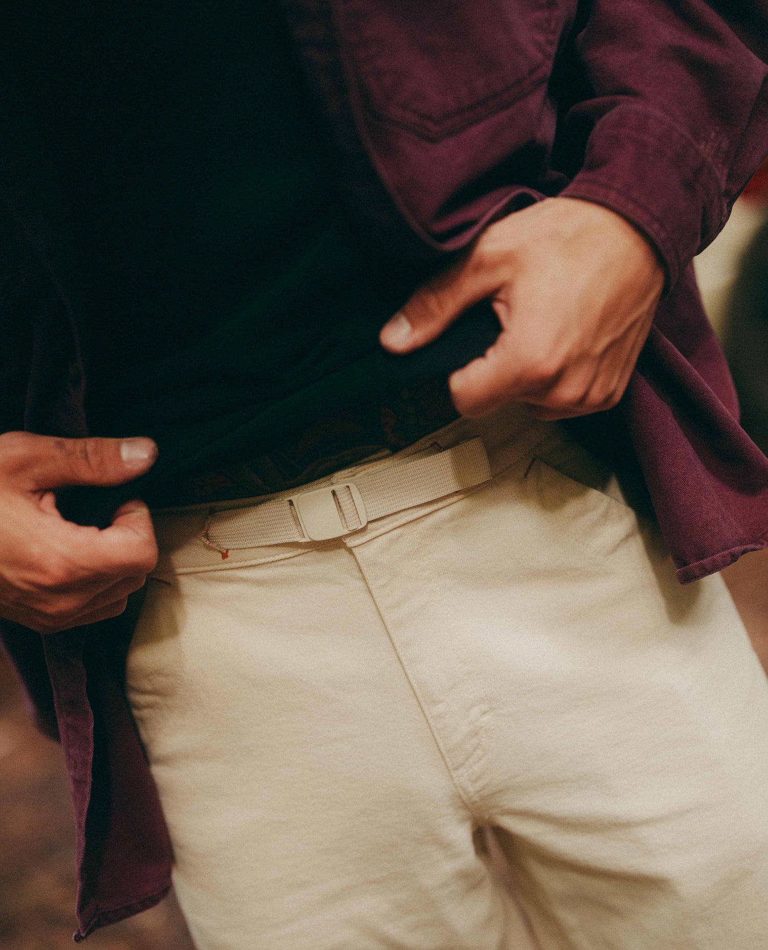 Person adjusting a belt with a focus on hands and clothing details.