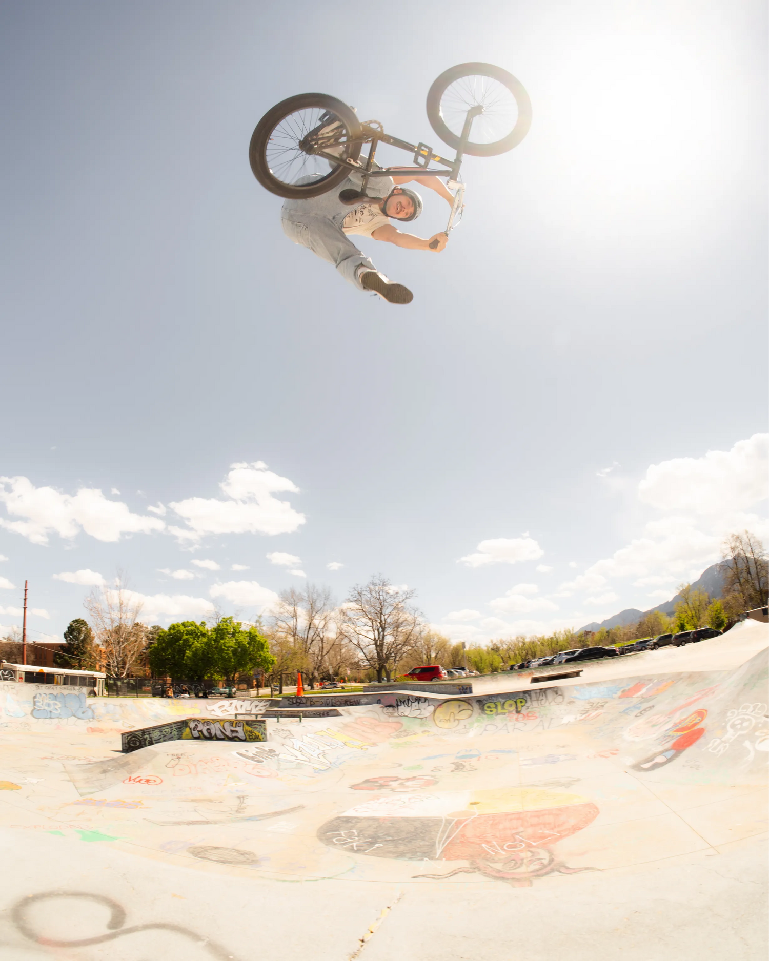 Person performing a bike trick in the air over a skate park with a clear sky.