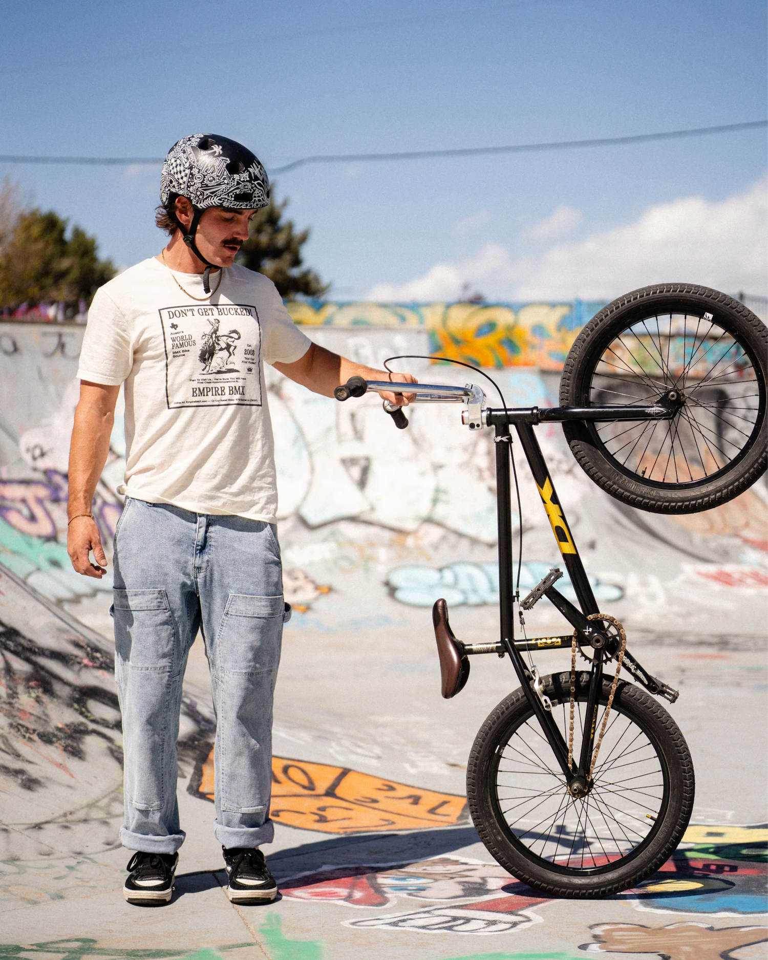 Person with a helmet and bike in a skate park with graffiti on the wall.