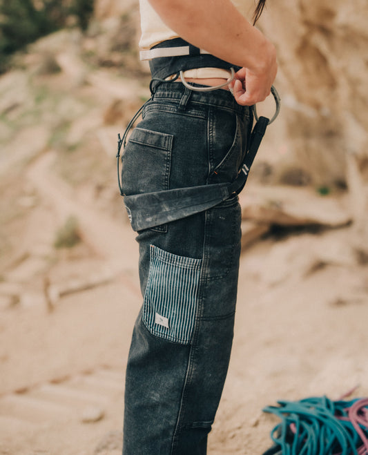 Photo of woman's legs outside in front of rock, waring navy pants with striped pocket and harness.