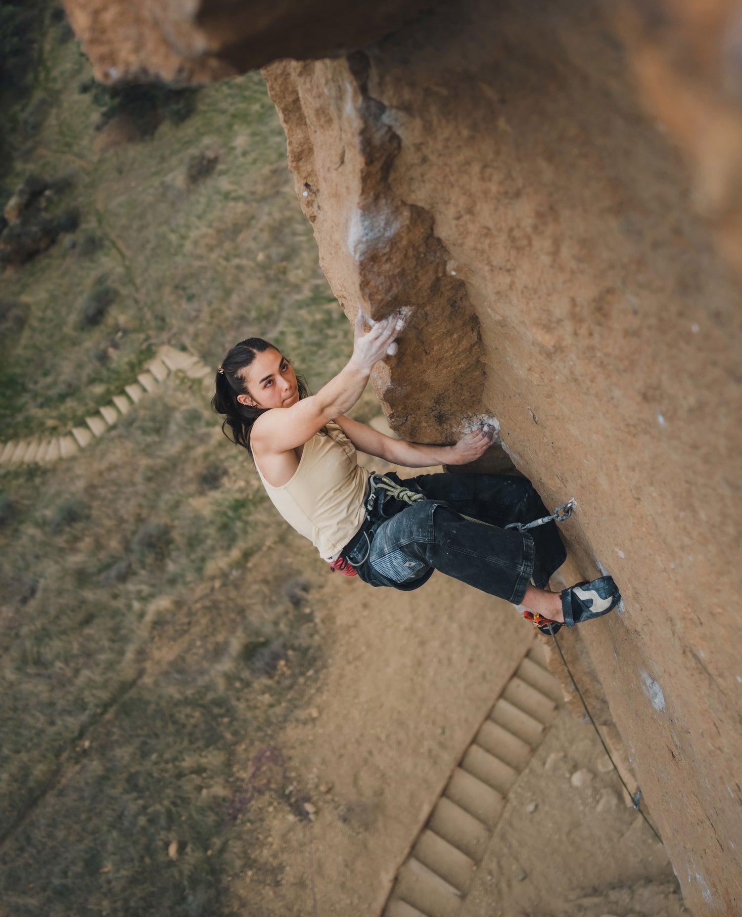Girl rock climbing outside, wearing yellow shirt and navy pants 