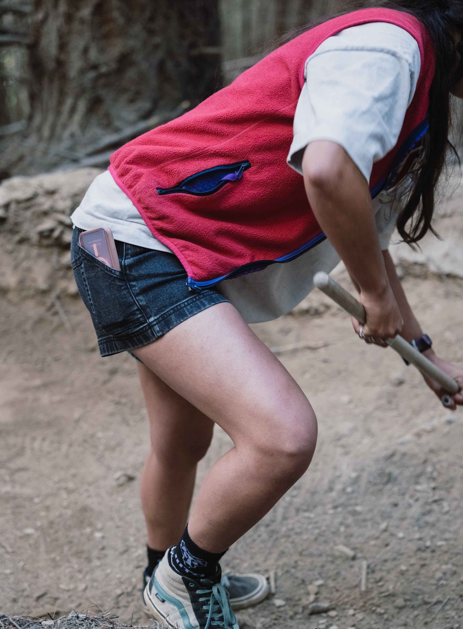 Close up of woman digging with shovel wearing red vest, white shirt, black shorts 