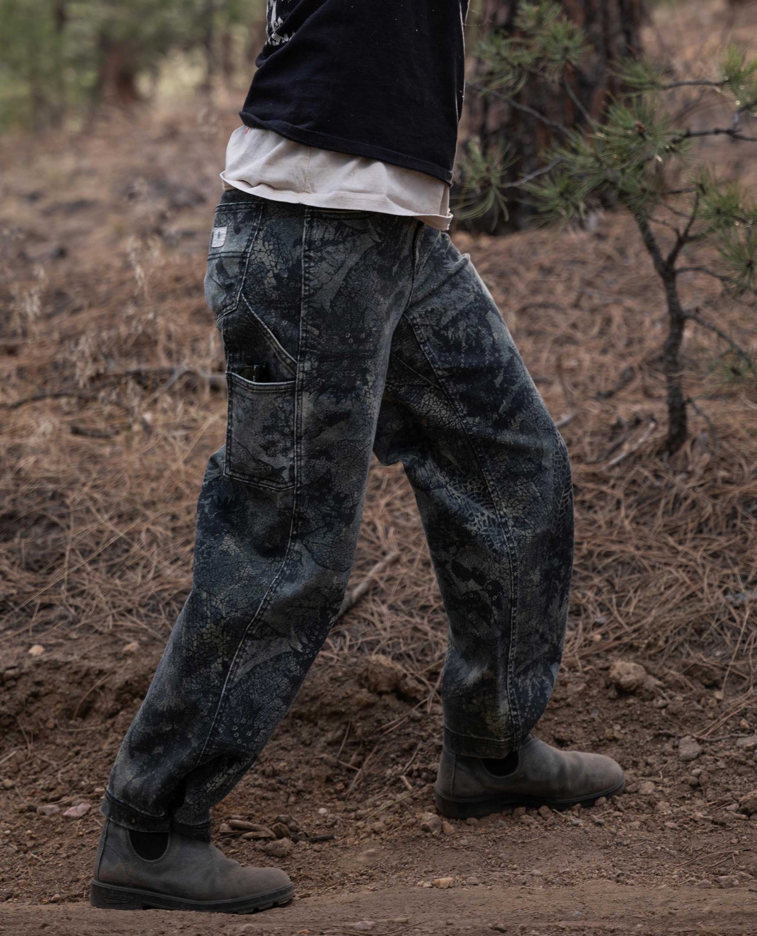 Camouflage leaf pants outside, in front of brown background. 