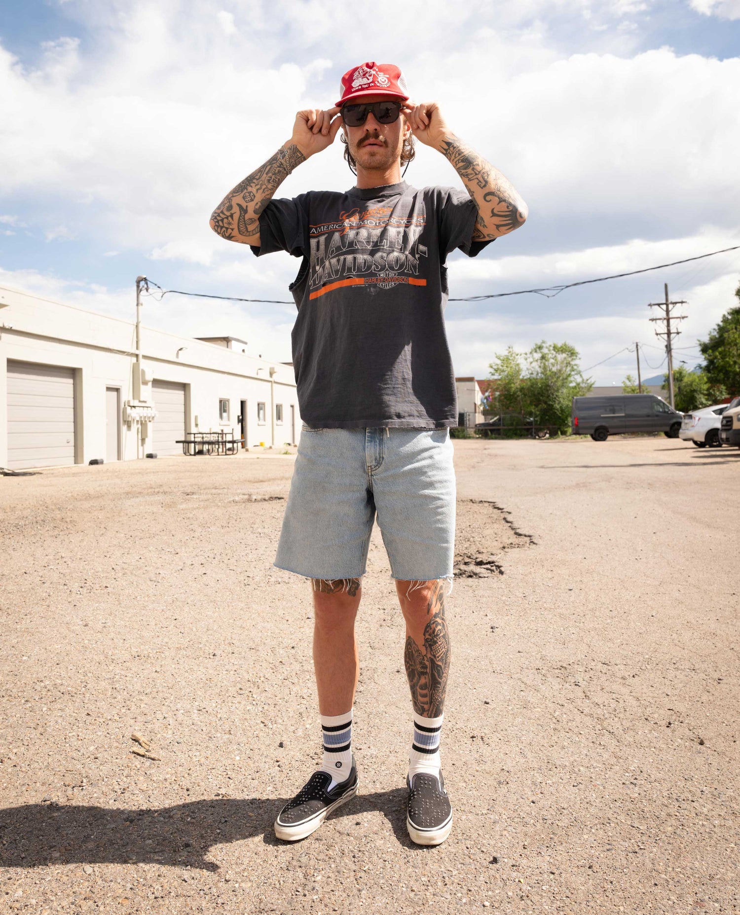 Man wearing a red cap, sunglasses, and casual clothing standing on a street.