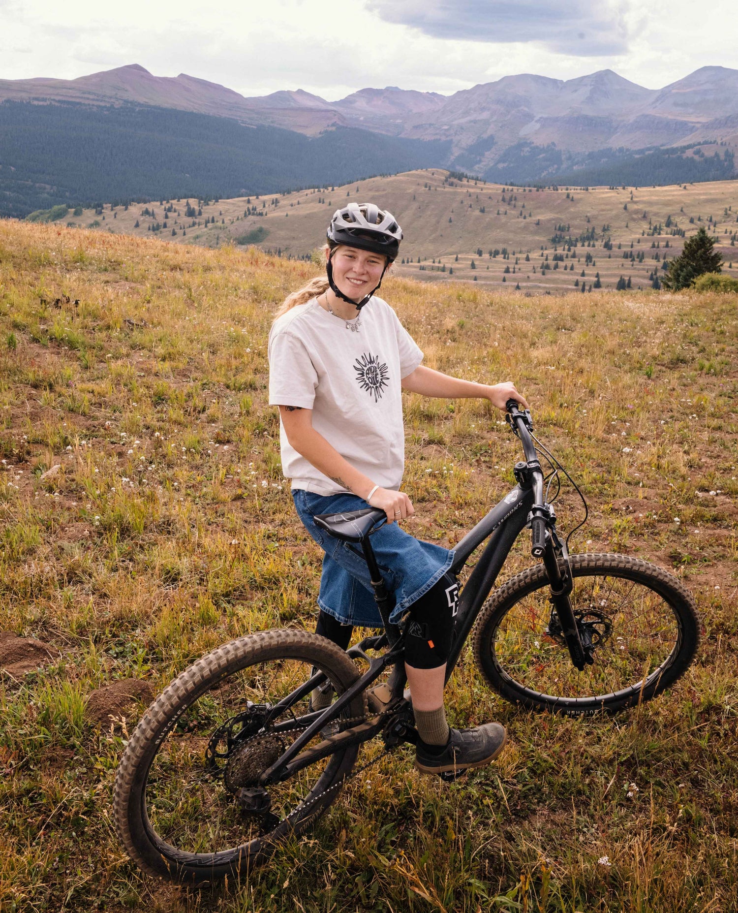 Lucy in Silverton on a mountain bike in a high alpine meadow with mountains in the background
