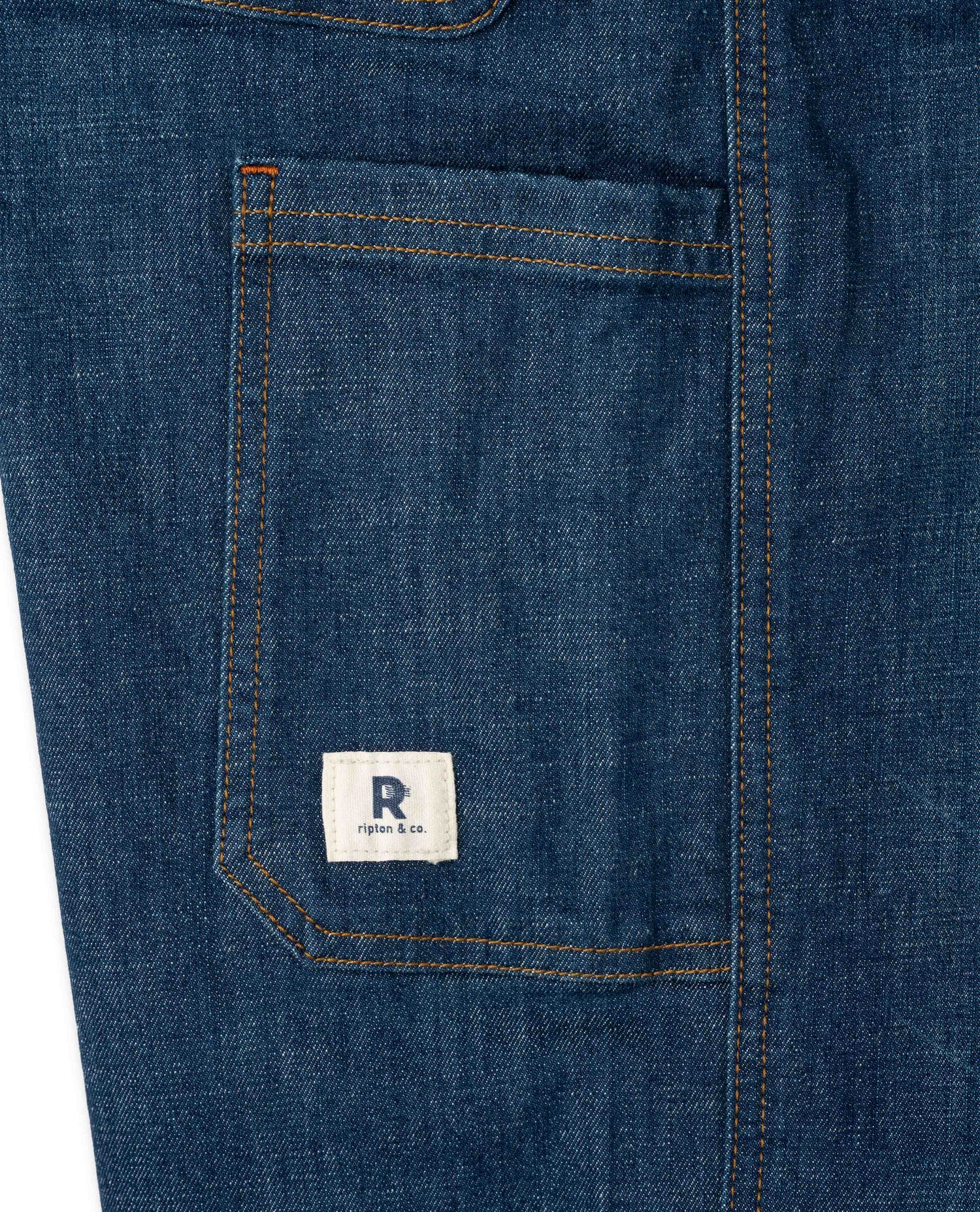 Close-up of a blue denim pocket with a brand logo on a white background