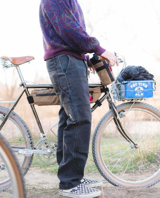 Man holding bike outside, wearing purple sweater and black pants with blue box on bike, 