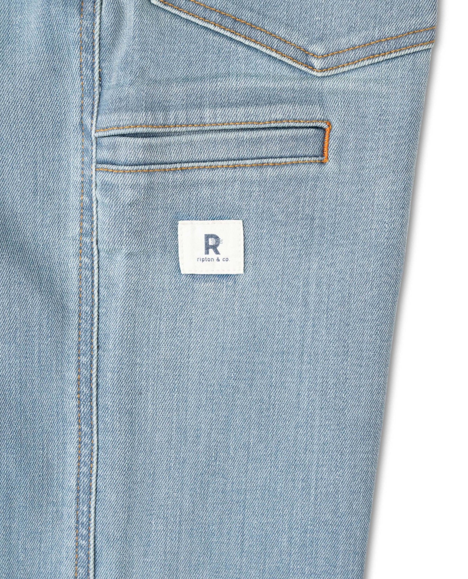 Close-up of a blue denim pocket with a brand label on a white background