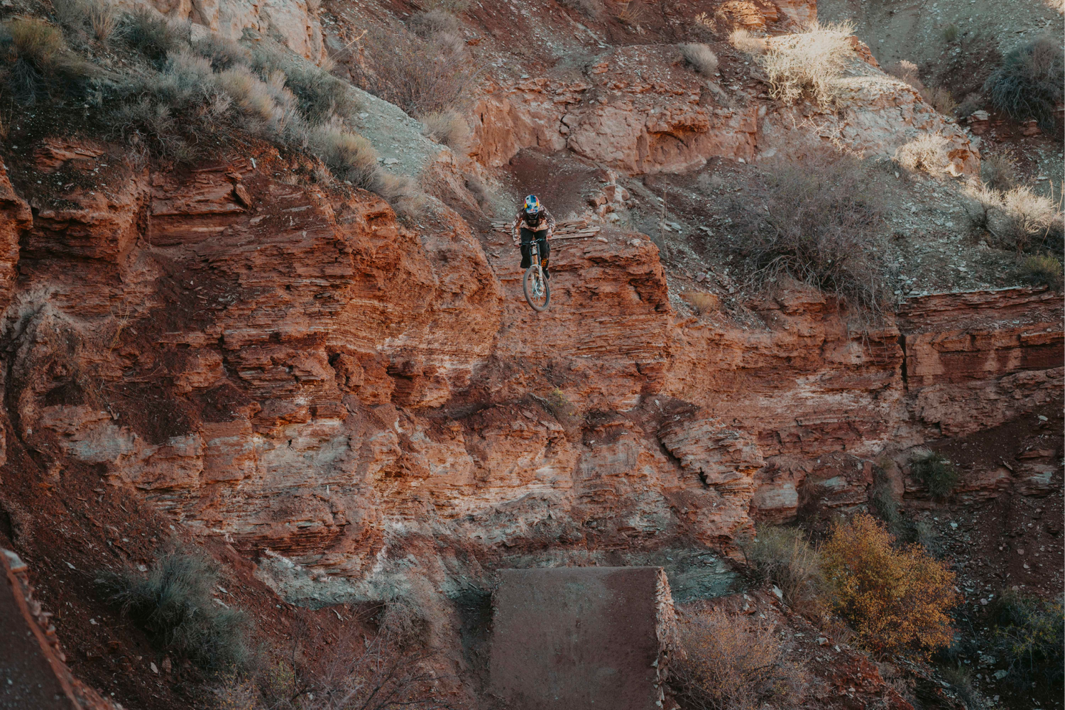 Person riding a mountain bike off a rocky cliff edge with a scenic landscape