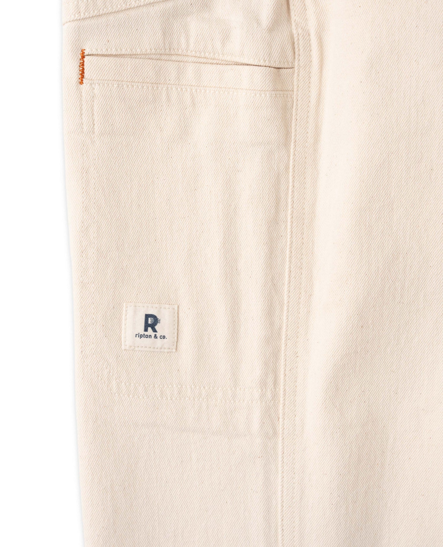Close-up of beige pants with a brand logo on the pocket