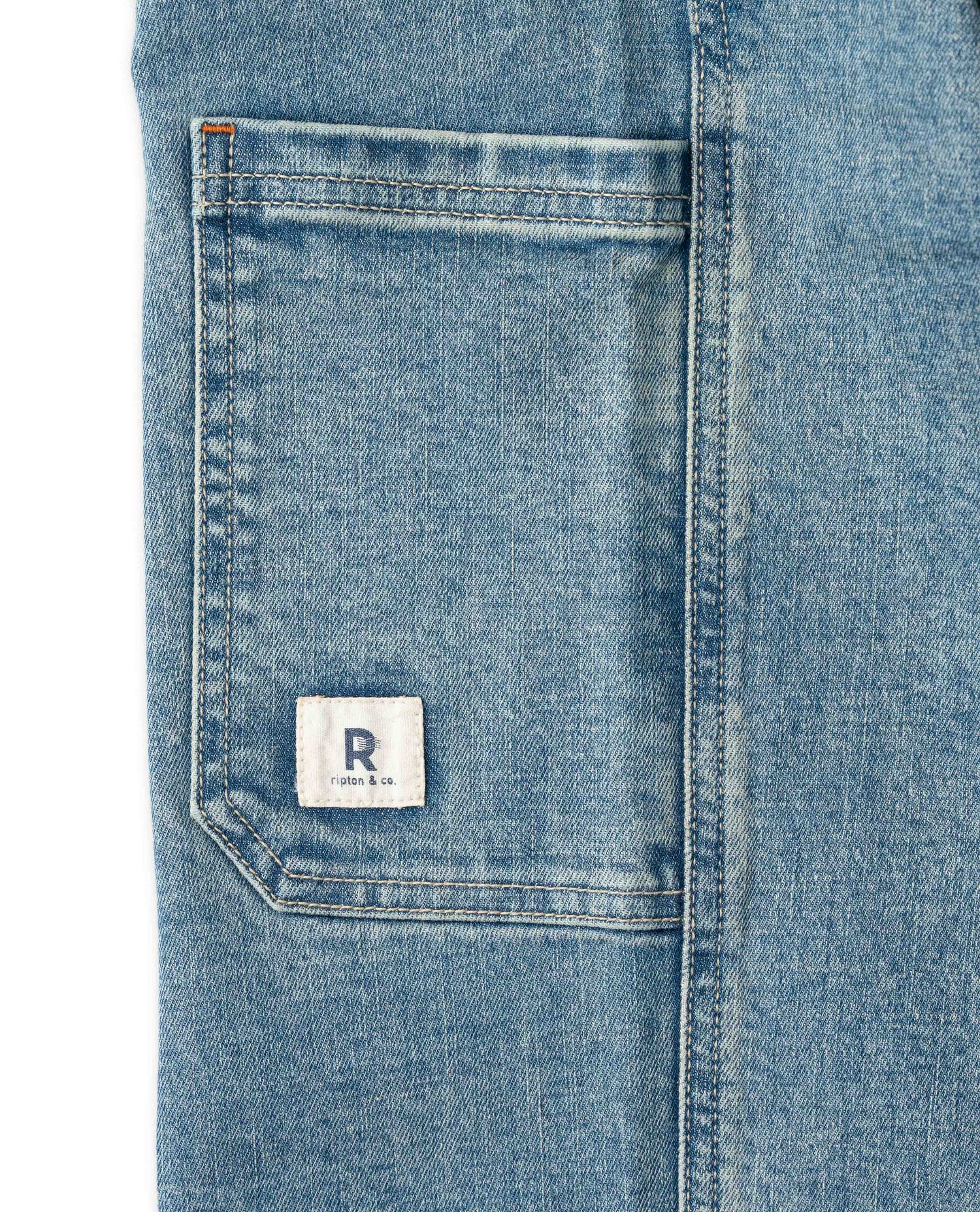 Close-up of a blue denim pocket with a brand logo on a white background