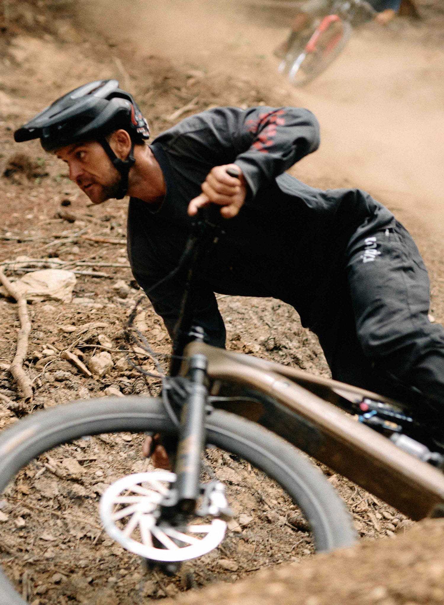 Biker in action on a dirt track wearing a helmet and black outfit.