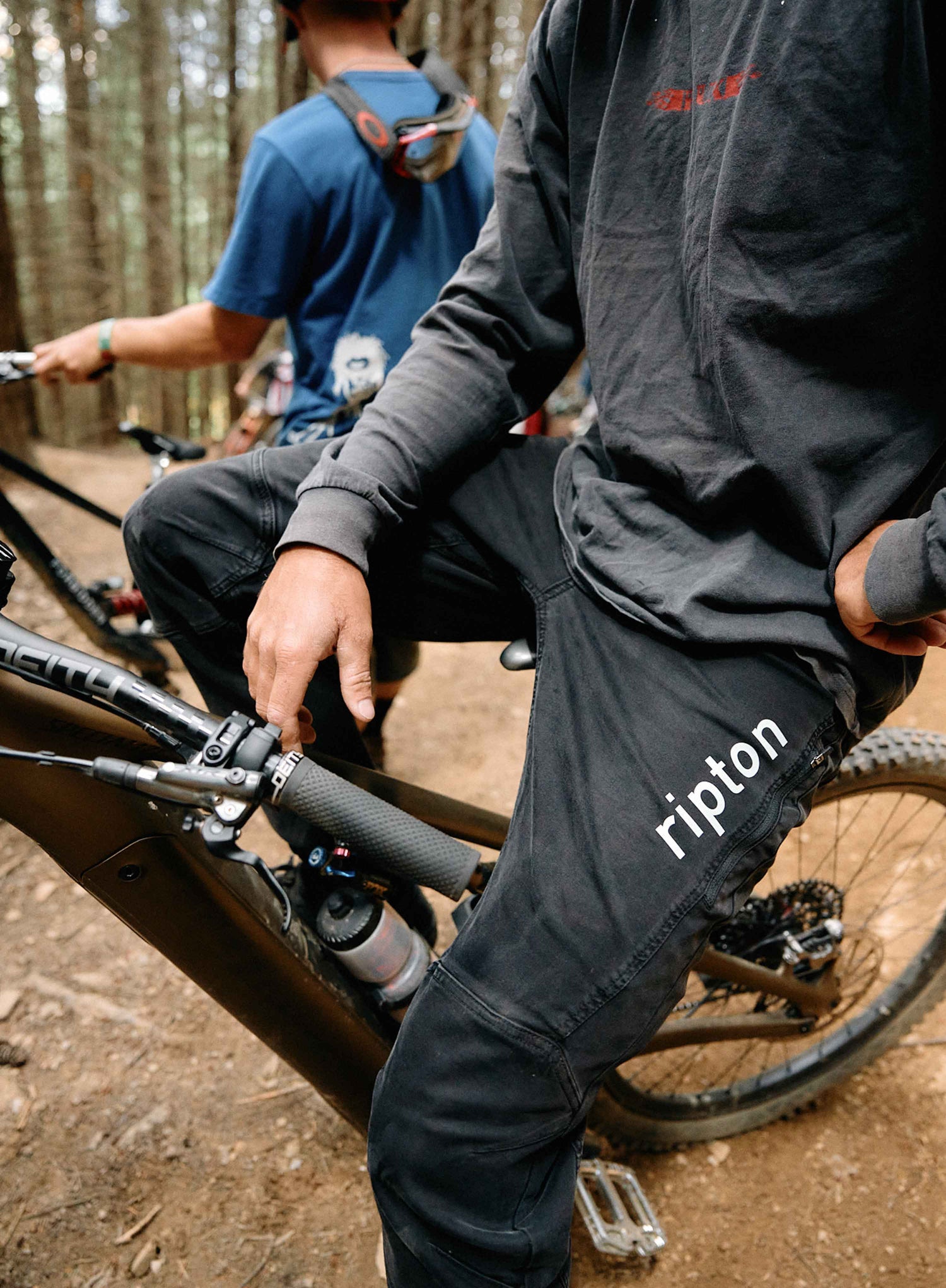 Two mountain bikers on a trail with one wearing 'ripton' pants.