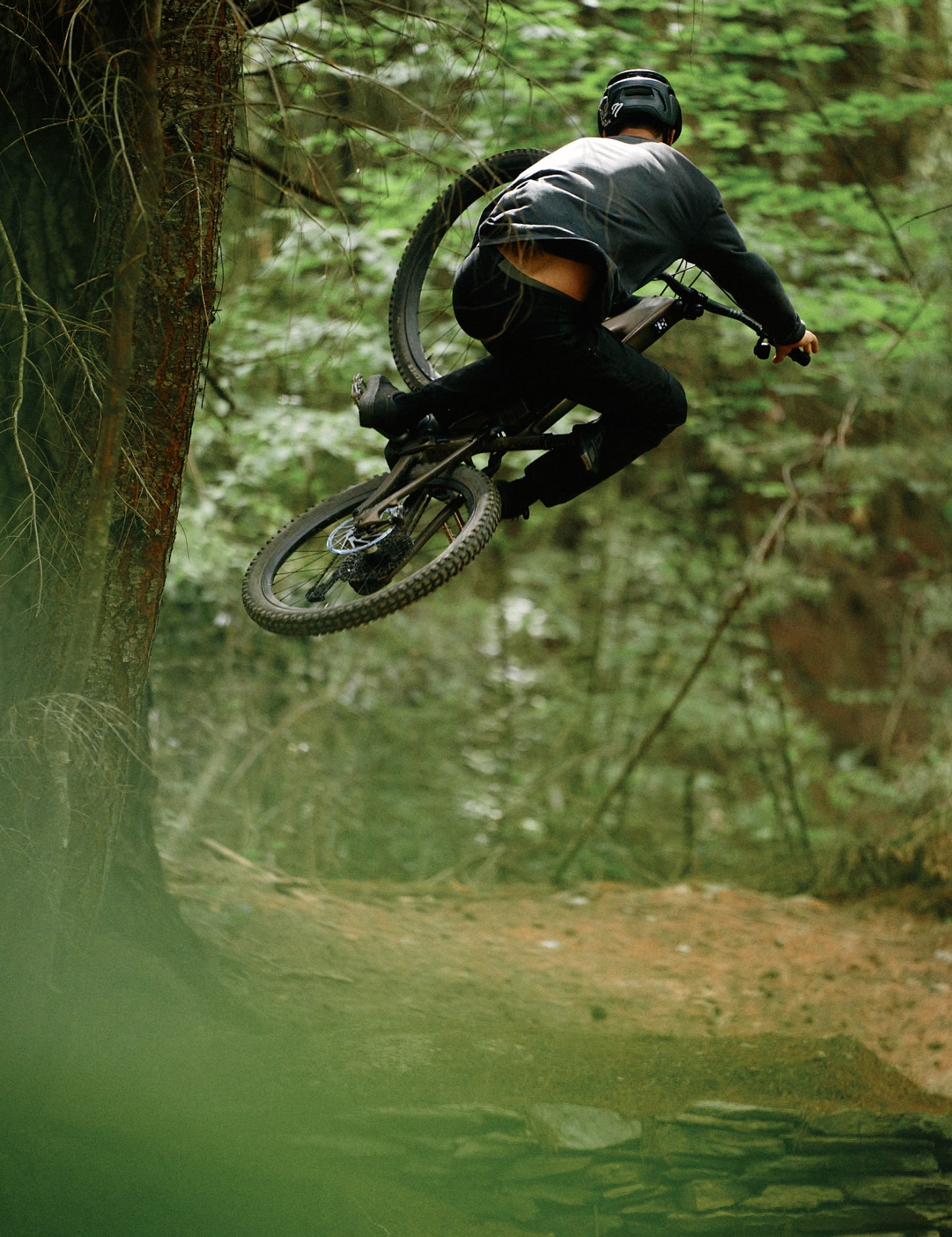 Person on a mountain bike in mid-air during a jump in a forest