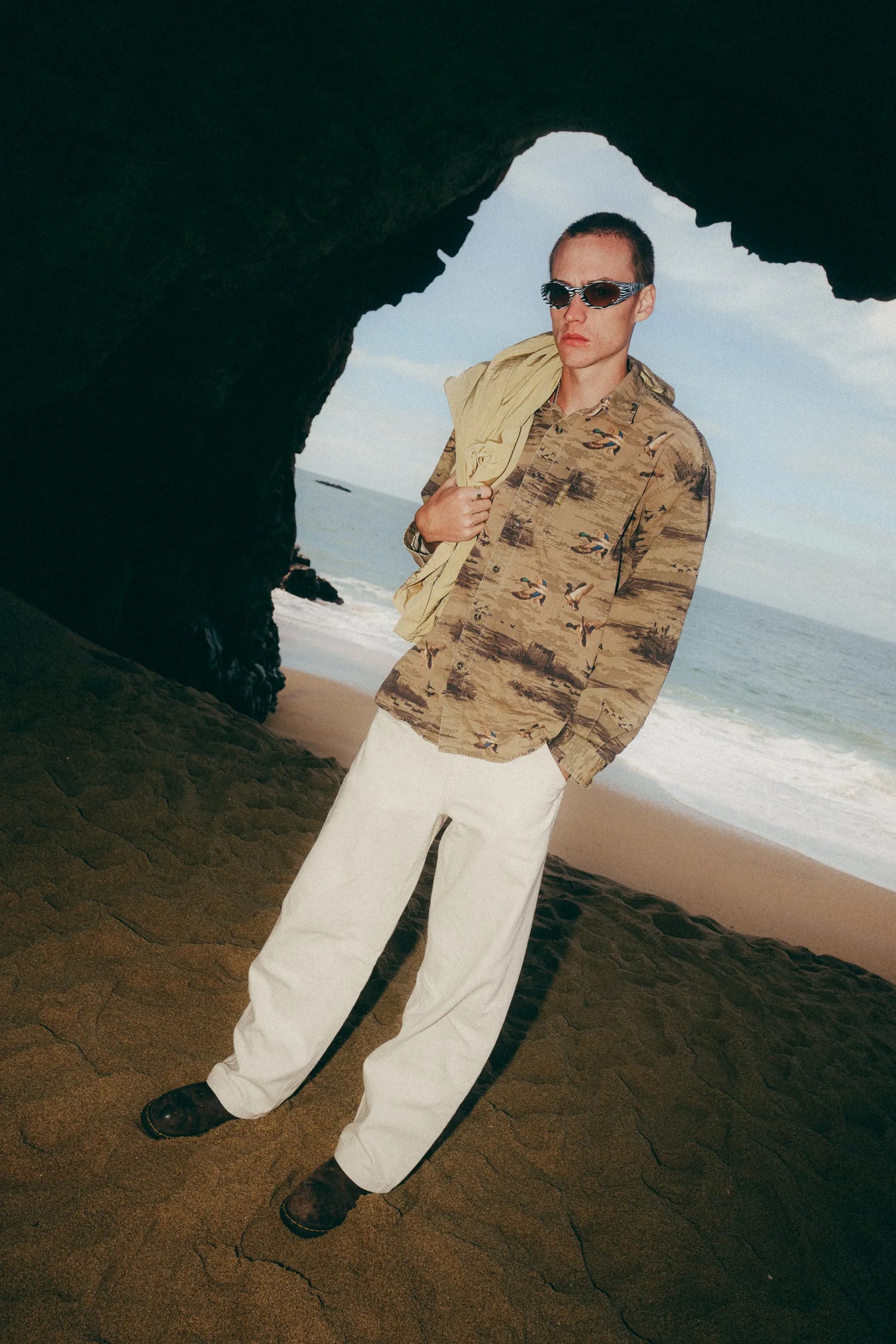 Person wearing a camouflage shirt and sunglasses with a beach scene in the background