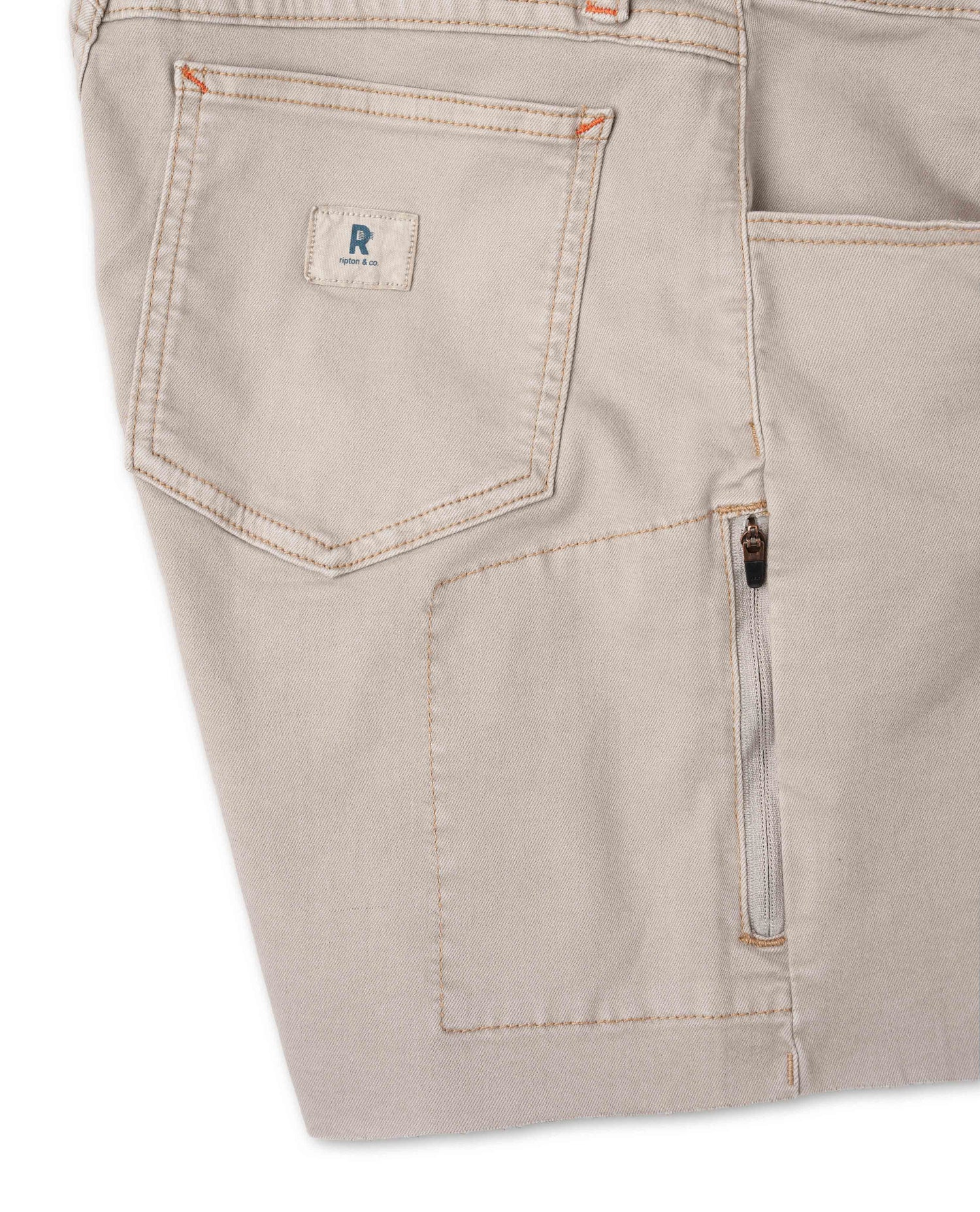 Close-up of beige pants with a brand logo on a white background